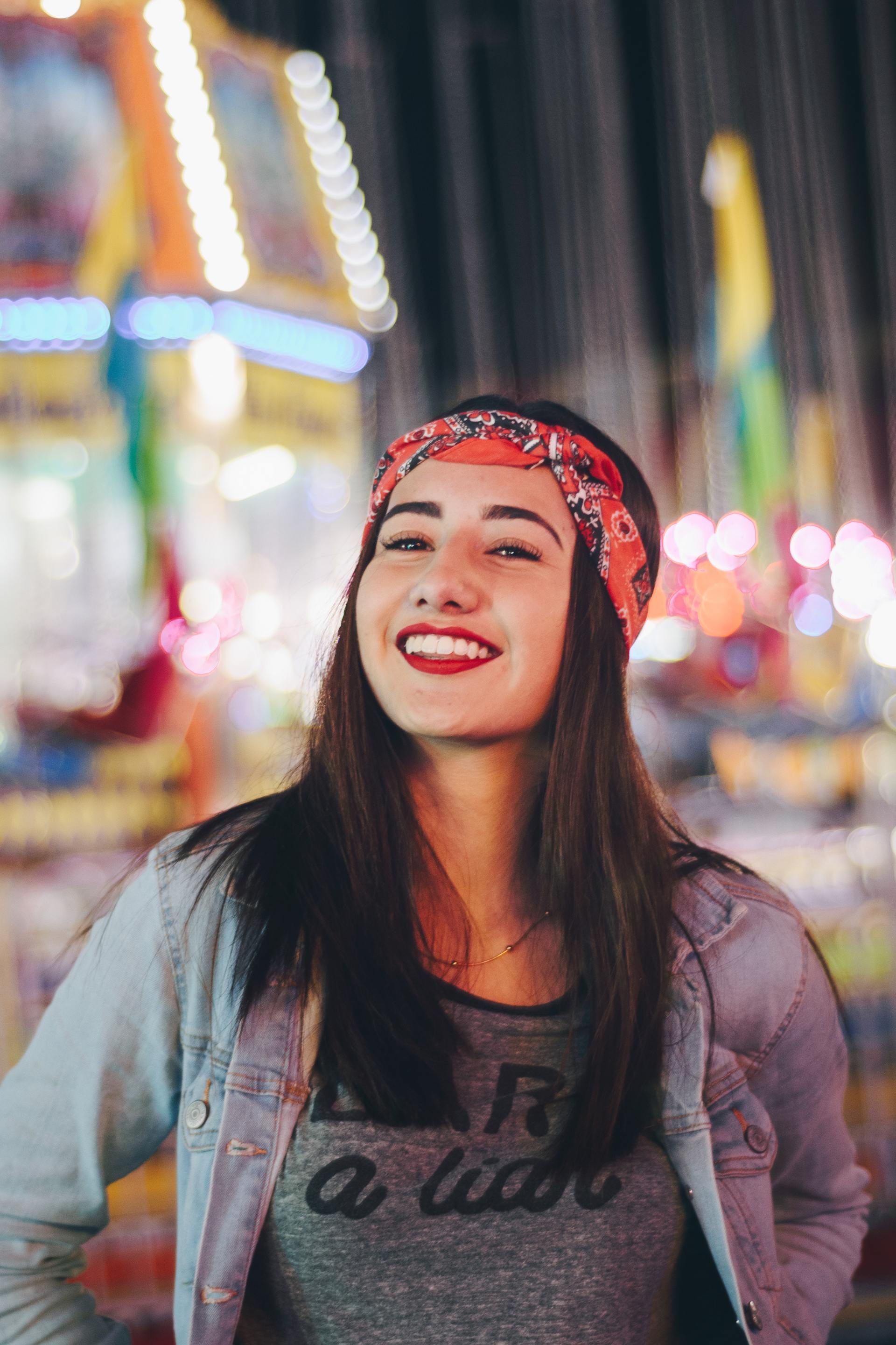 A girl wearing a bandana and red lipstick is smiling at a carnival.