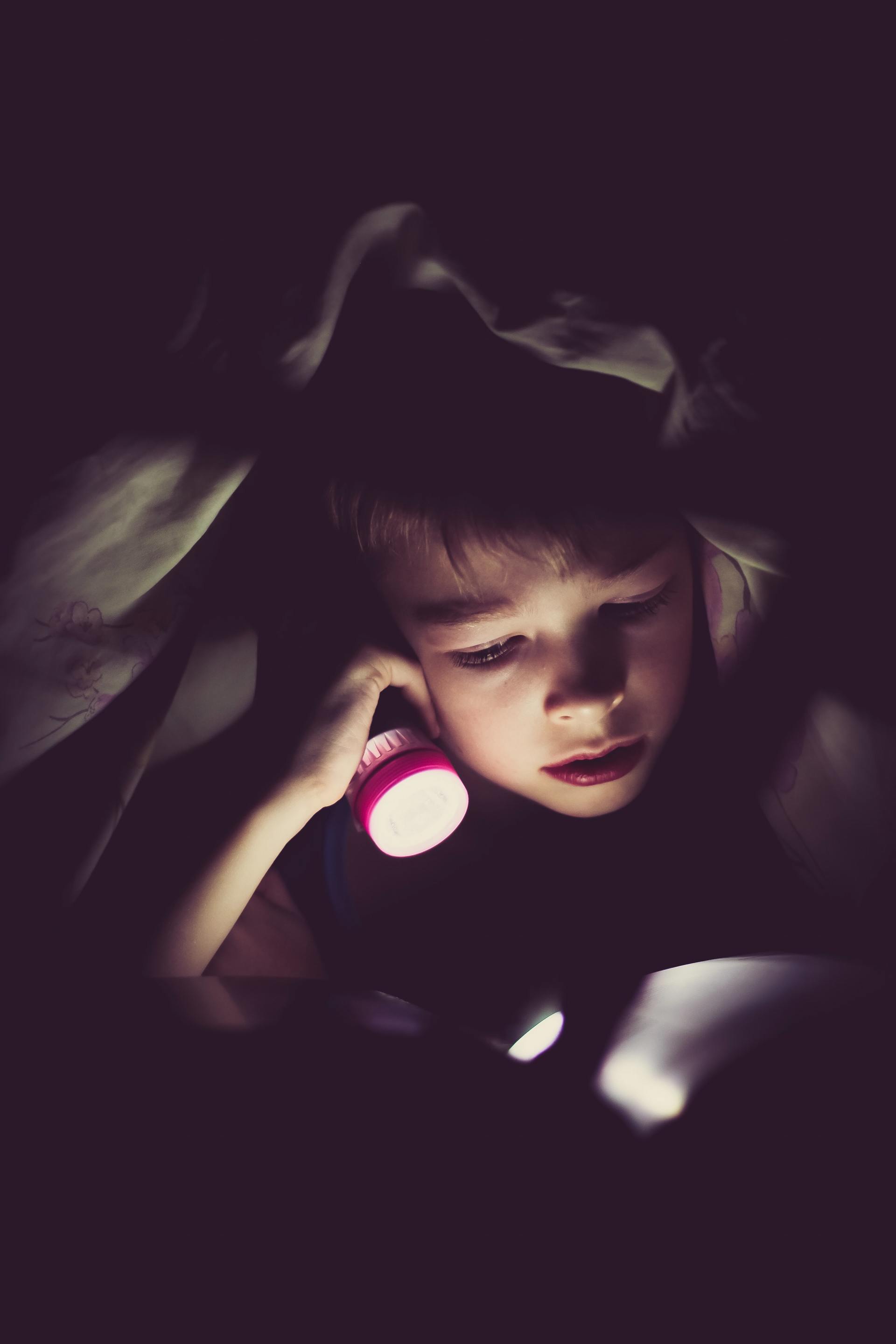 child using a torch in bed, in a dark room.