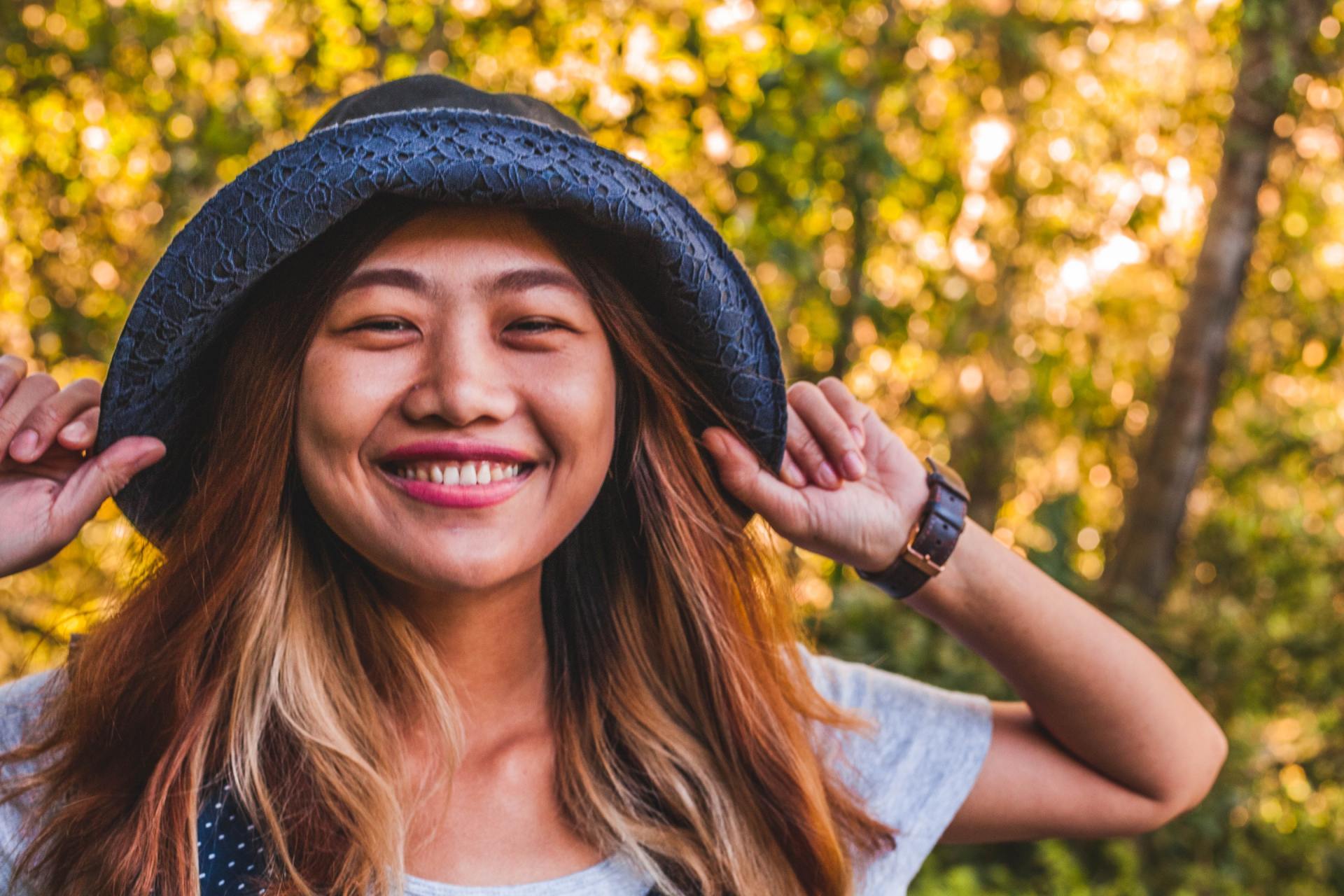 Asian young woman posing with a hat and smiling outdoors