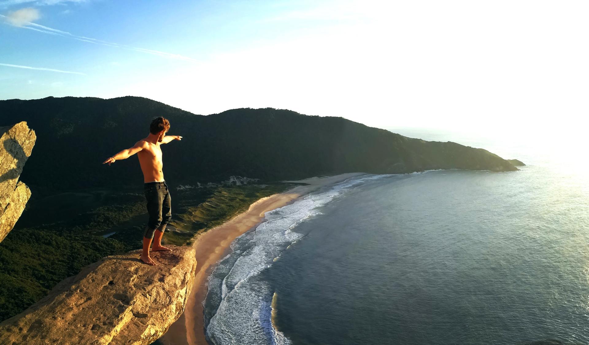 Um homem está parado na beira de um penhasco com vista para o oceano.