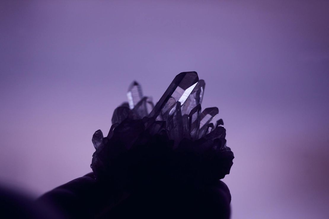 A person is holding a crystal in their hand on a purple background.