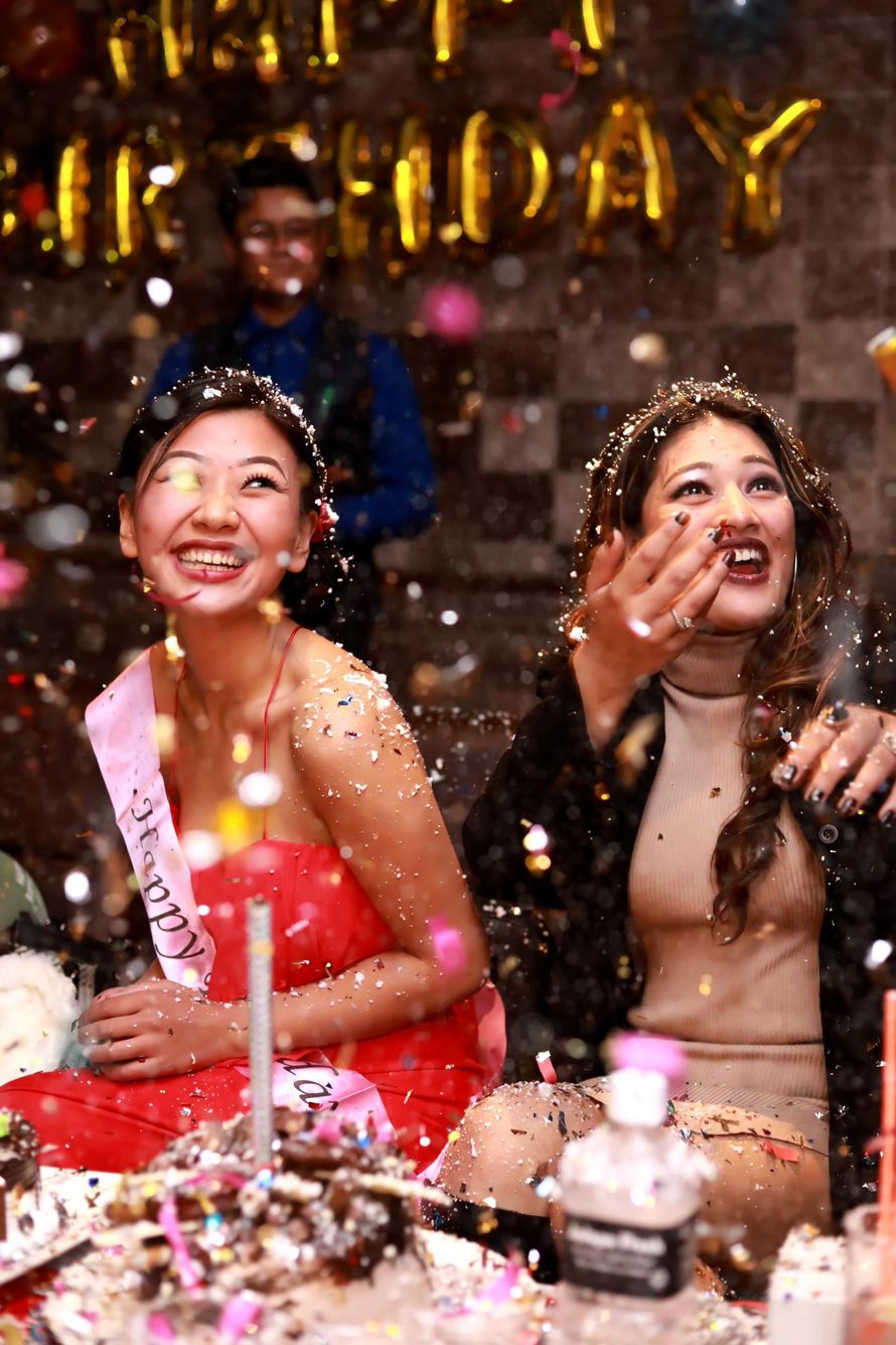 Two women are sitting at a table with confetti falling around them.