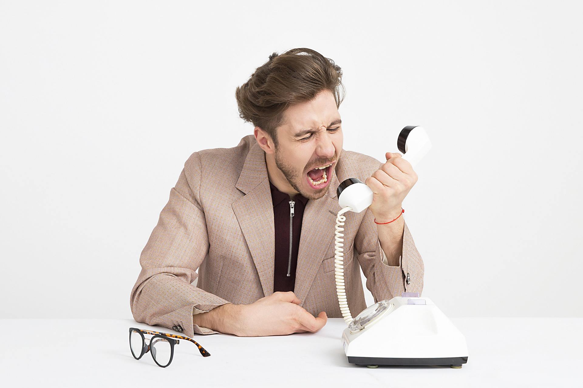 a man is sitting at a desk screaming into a telephone .