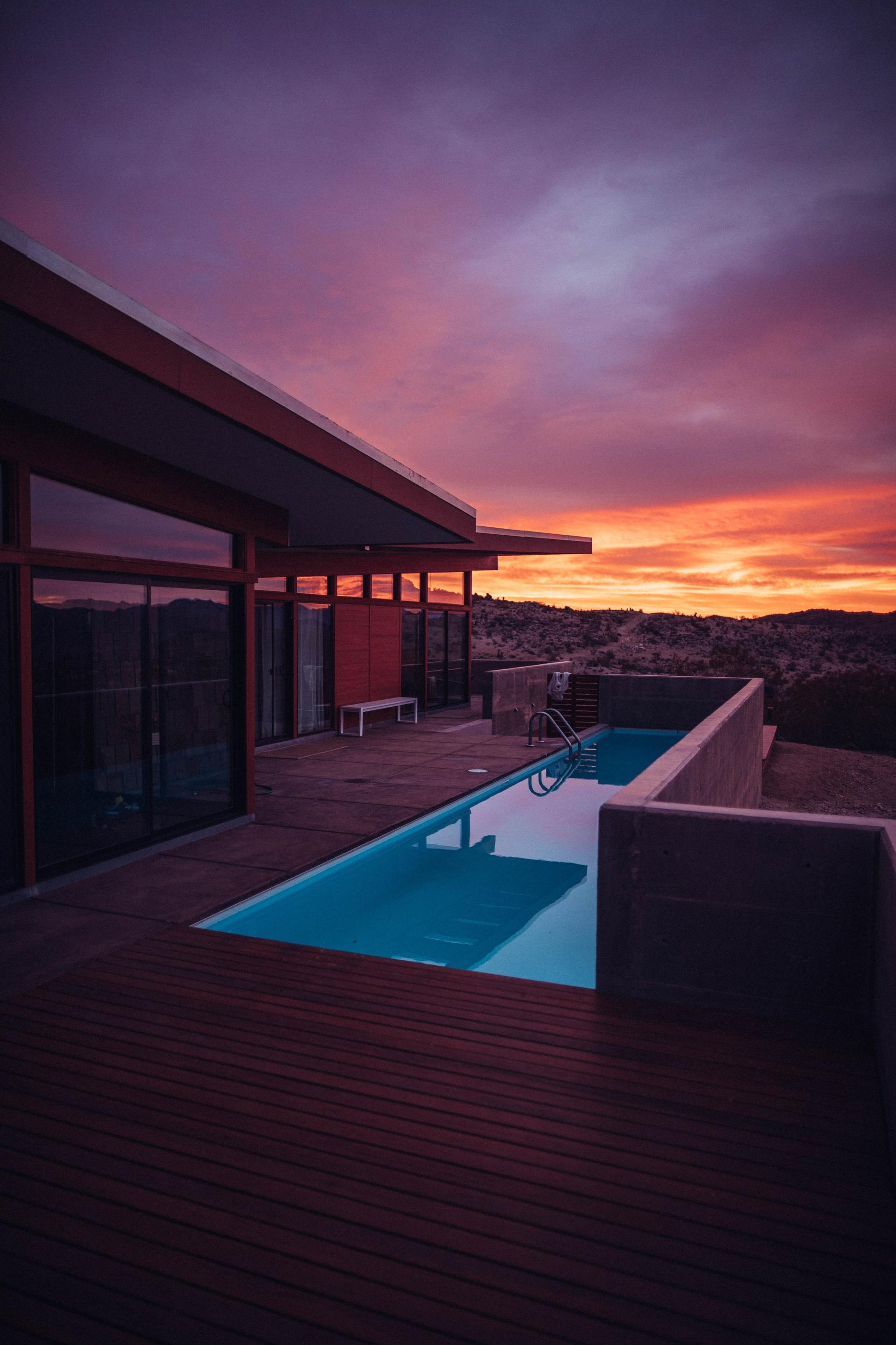 A house with a swimming pool in front of it at sunset.