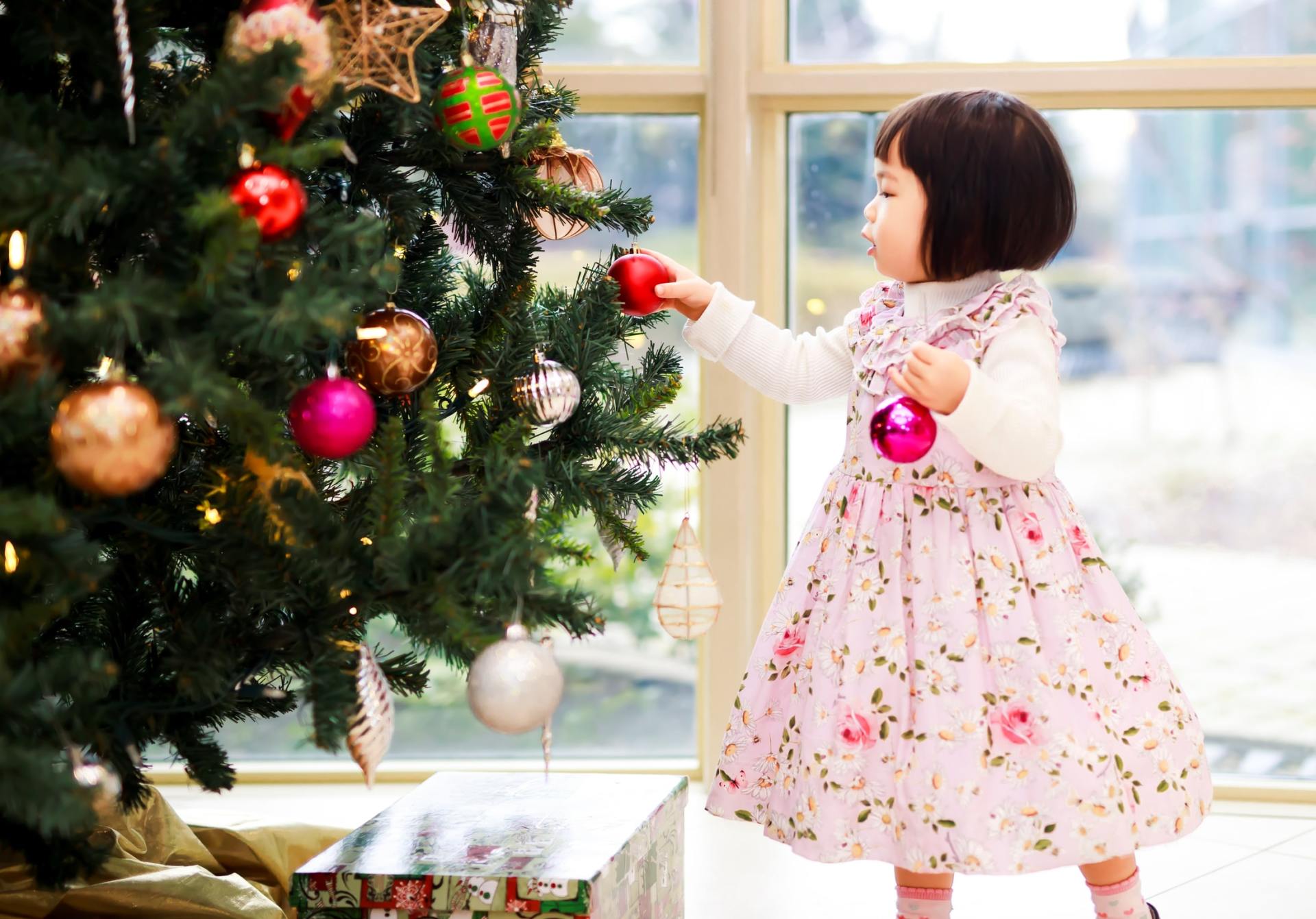 A little girl in a pink dress is decorating a christmas tree.