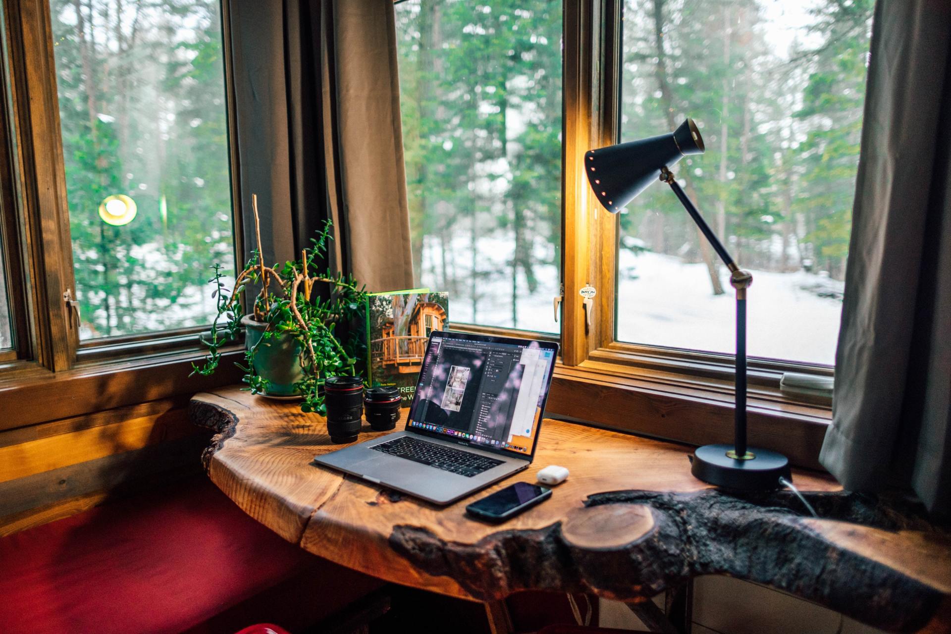 A laptop computer is sitting on a wooden desk in front of a window.
