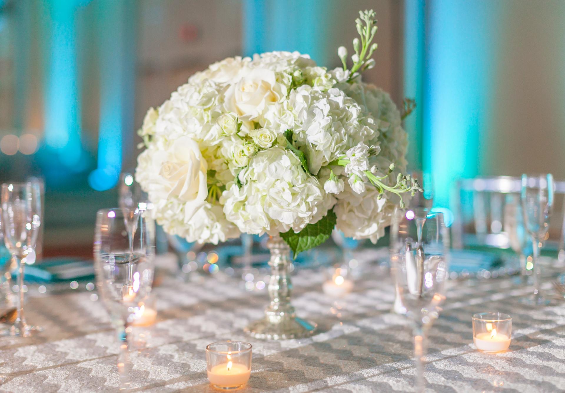 White floral centerpiece on a table set for an event with candles and glassware.