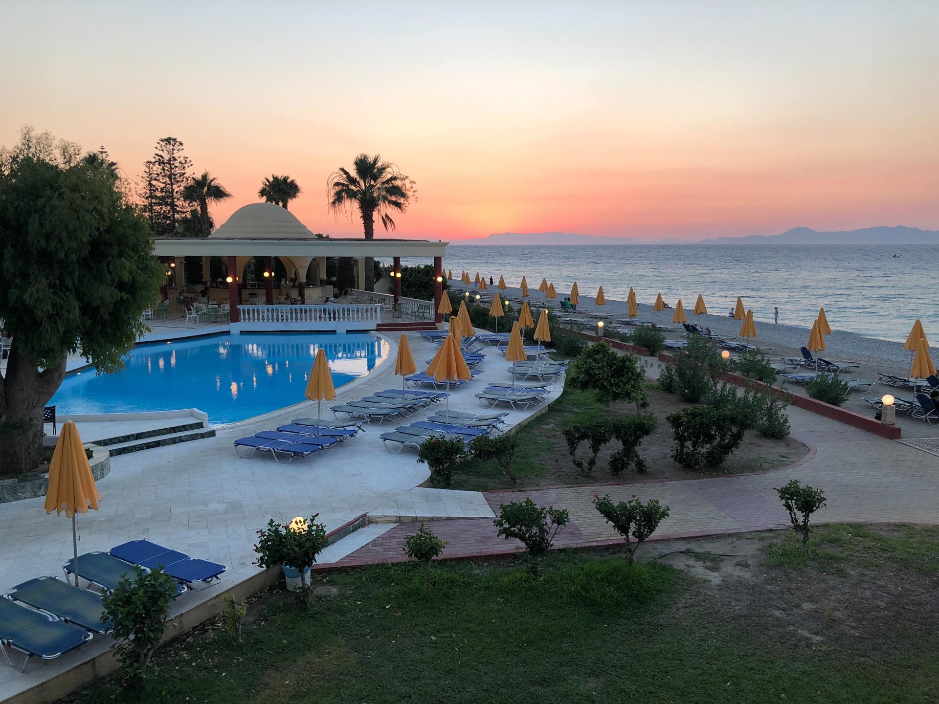 A large swimming pool surrounded by chairs and umbrellas with a sunset in the background,  life coach training, the coaching guild