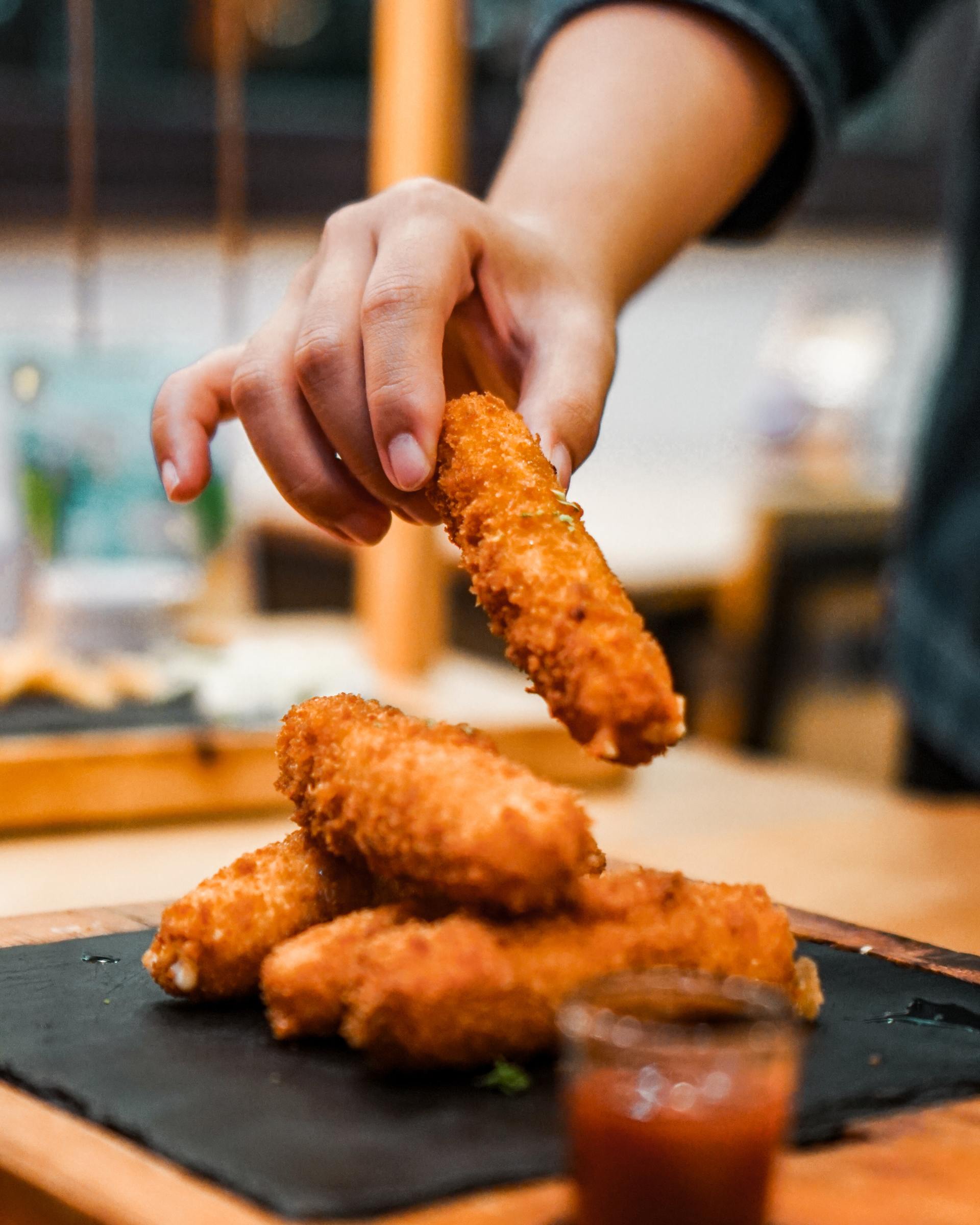 A person is dipping a piece of fried food in ketchup