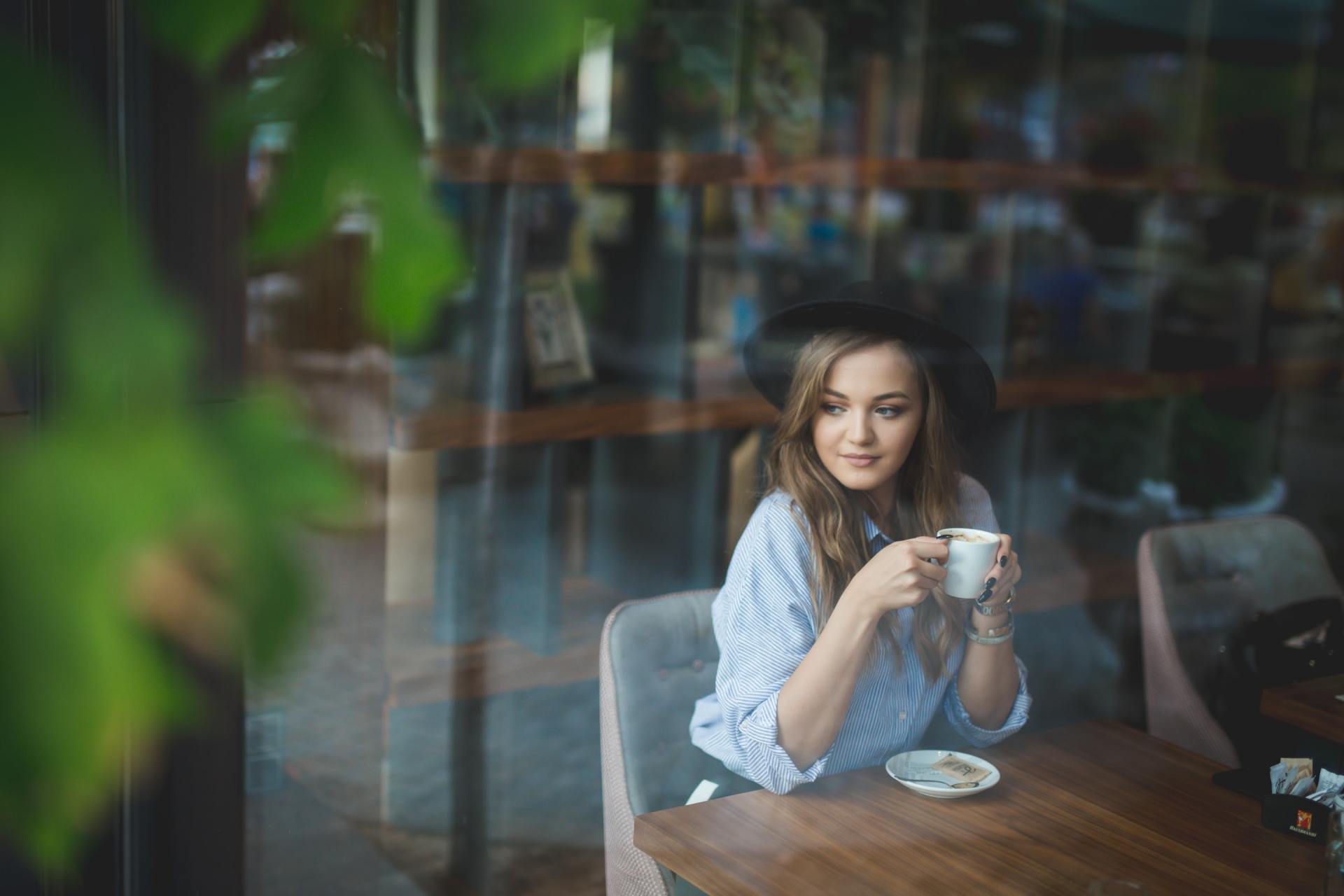 A woman is sitting at a table drinking a cup of coffee.