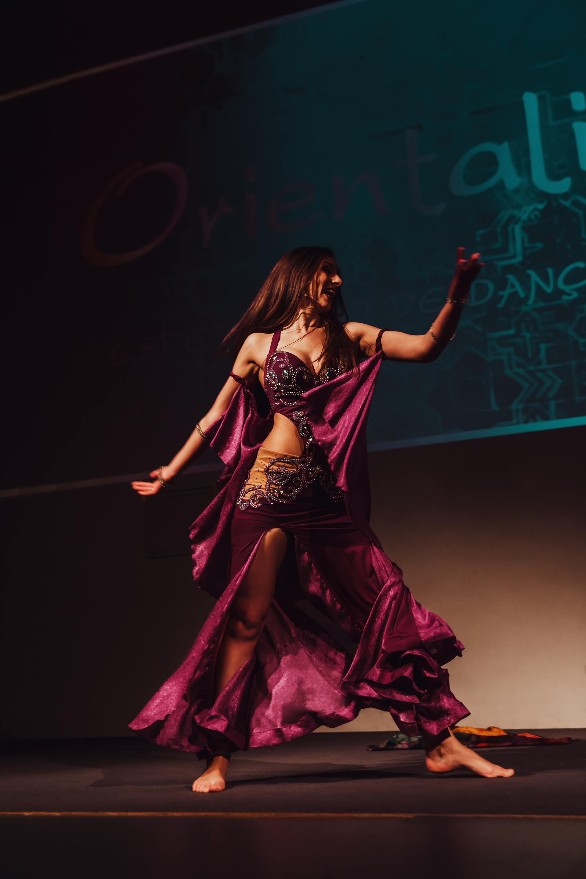 A belly dancer in a purple dress is dancing on a stage.
