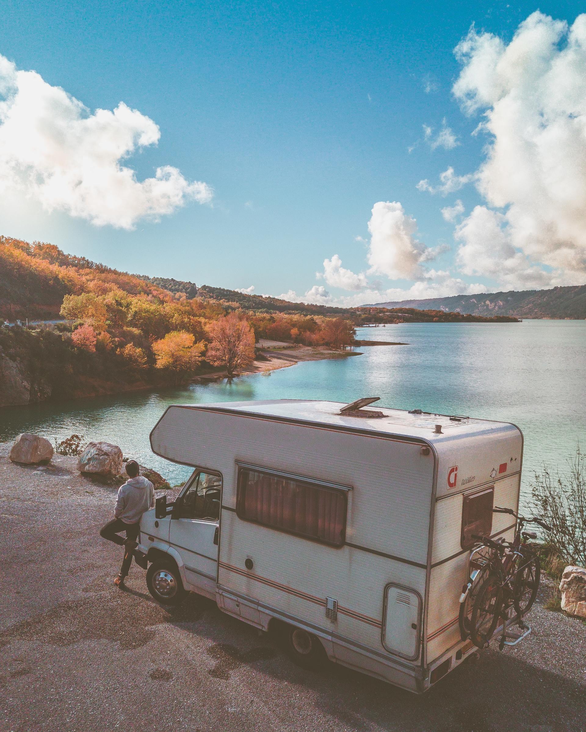 A camper van is parked by a tranquil lake surrounded by colorful autumn foliage.