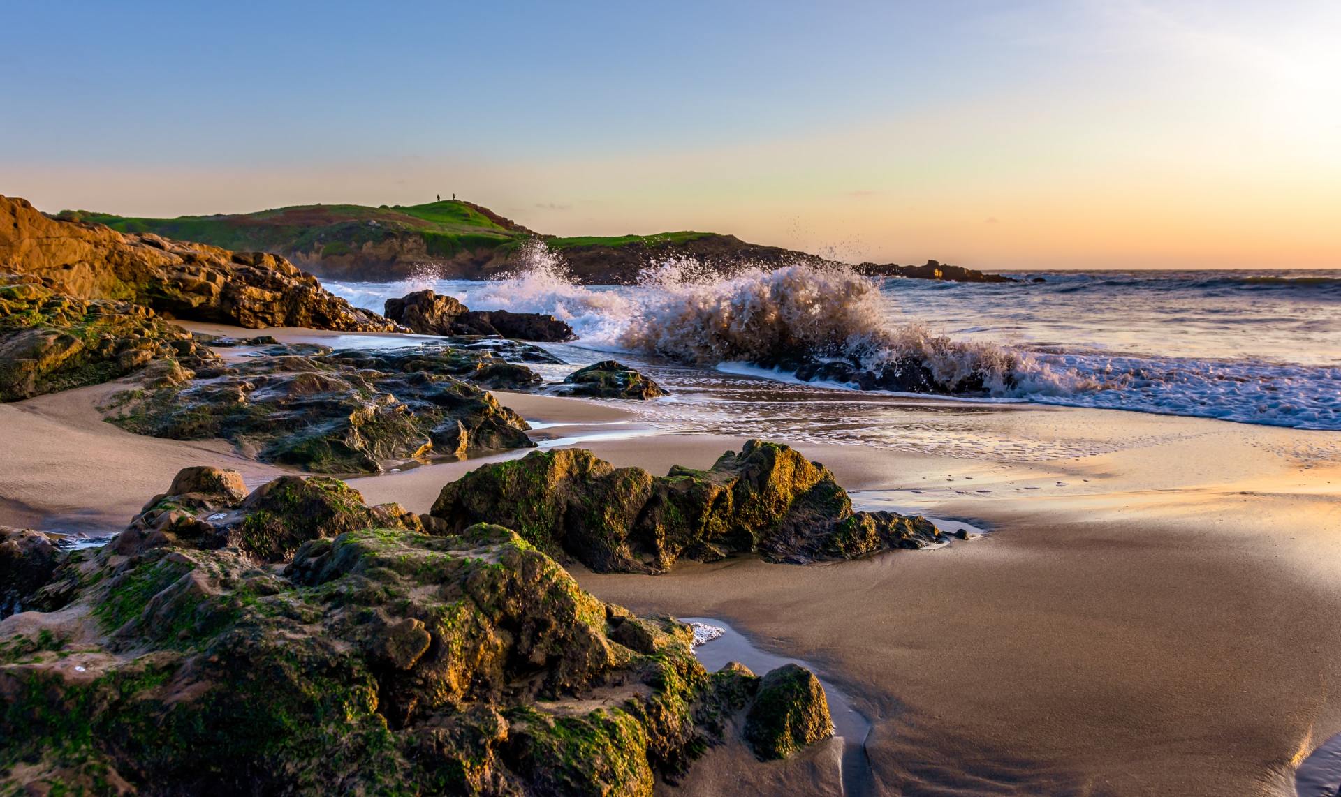 The waves are crashing against the rocks on the beach at sunset.