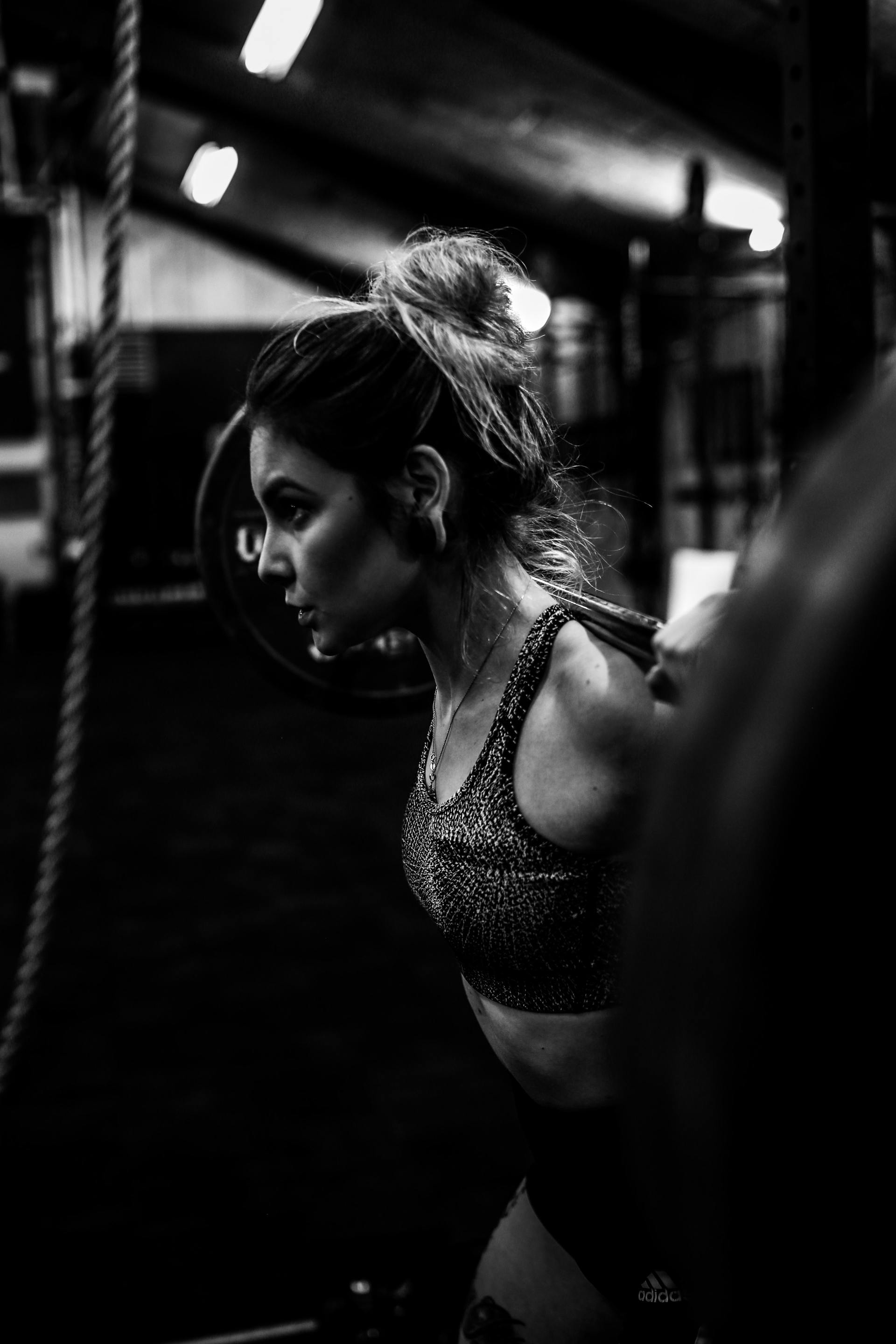 Een zwart-witfoto van een vrouw die met een halter in een sportschool hurkt.