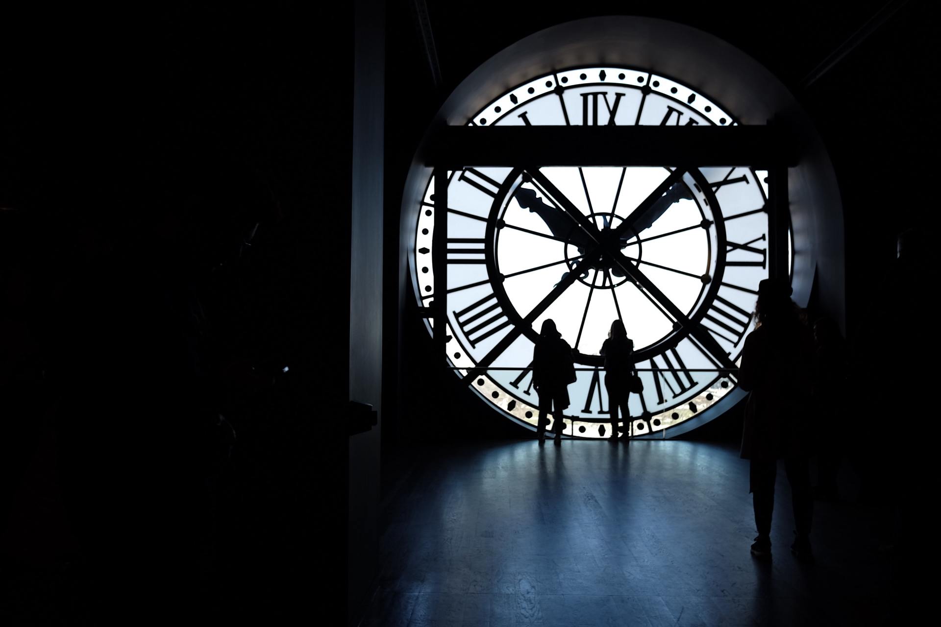 Silhouetted figures stand before a giant clock, in a dark interior.