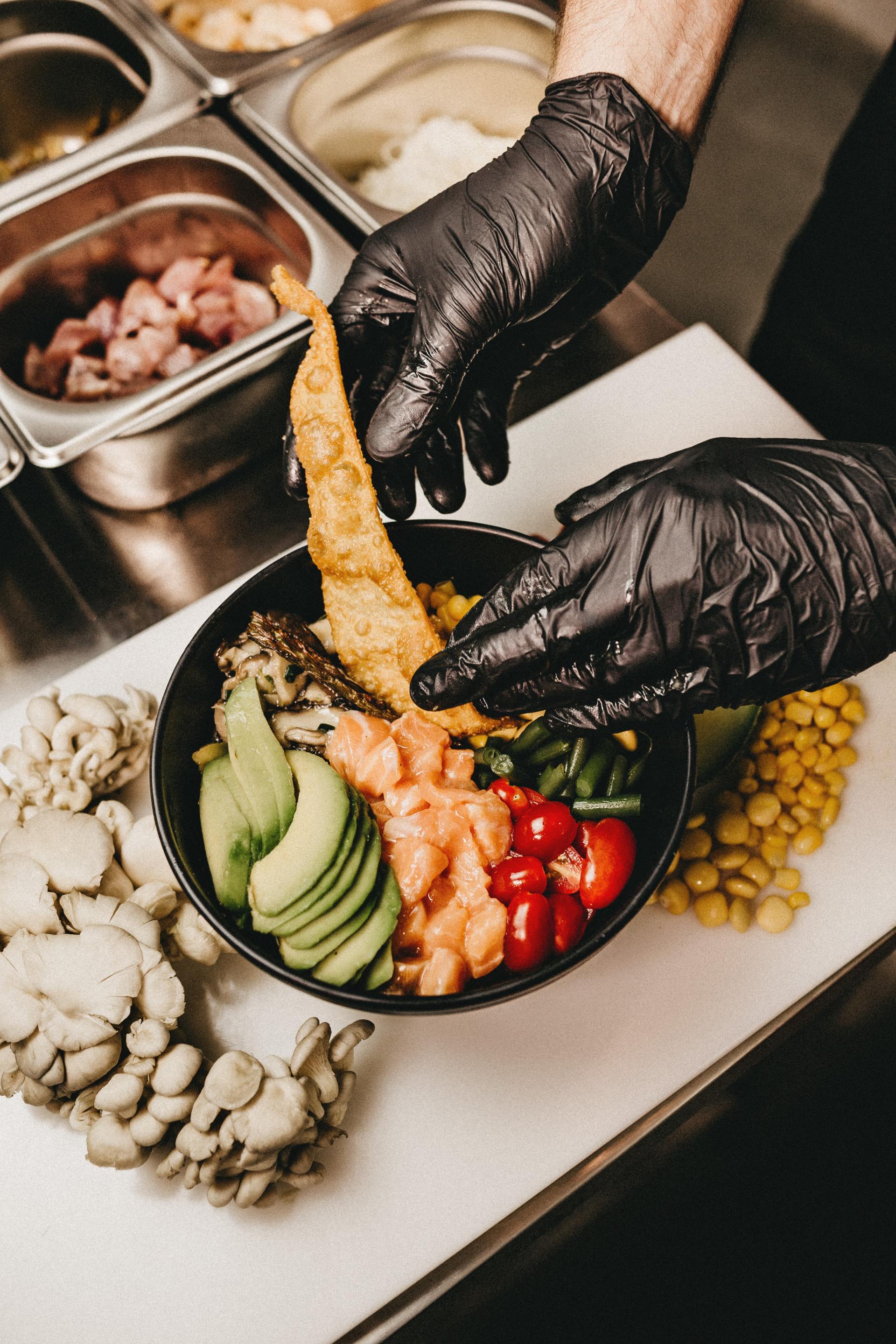 A person wearing black gloves is preparing a bowl of food