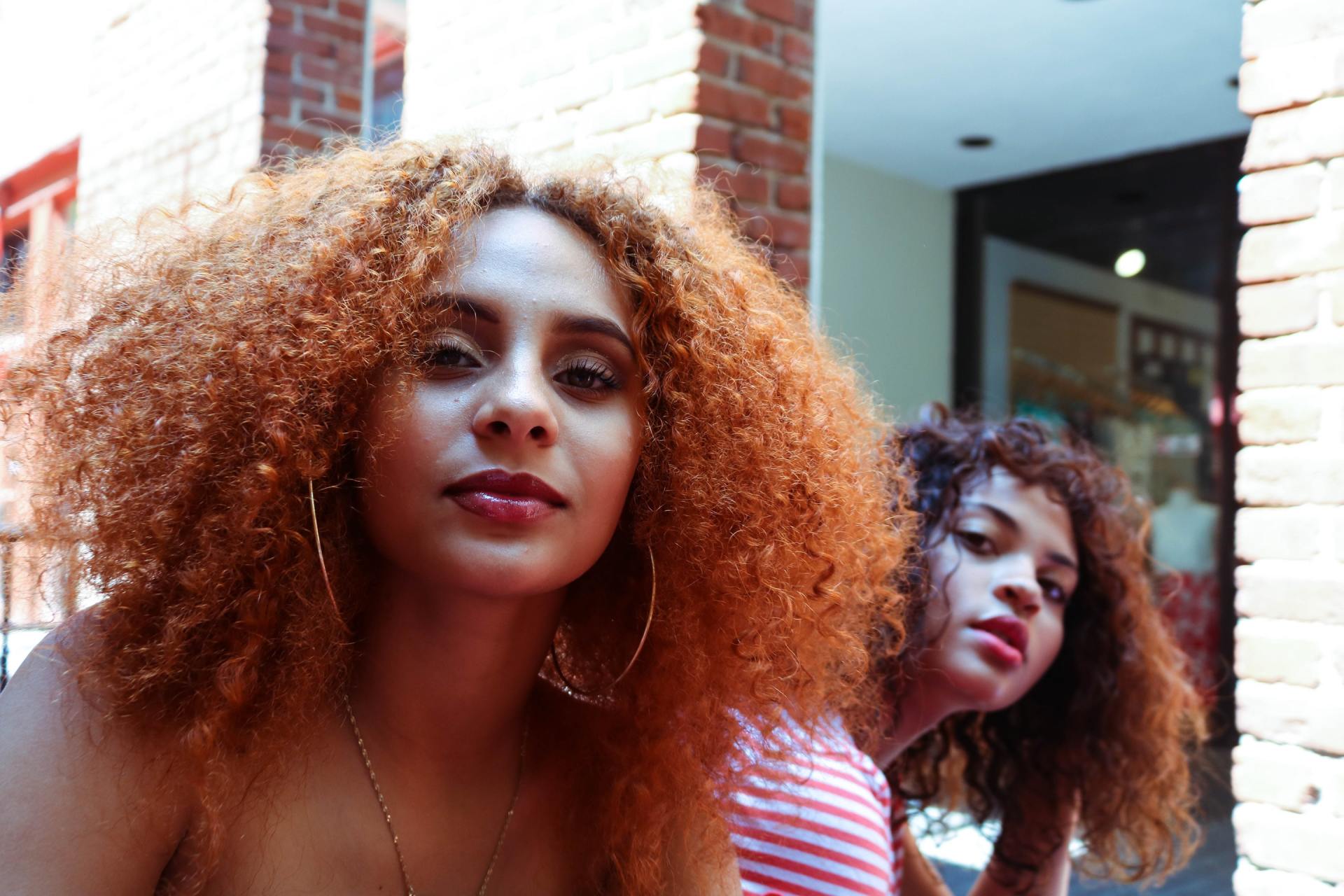 Two women with red curly hair are sitting next to each other in front of a brick wall.