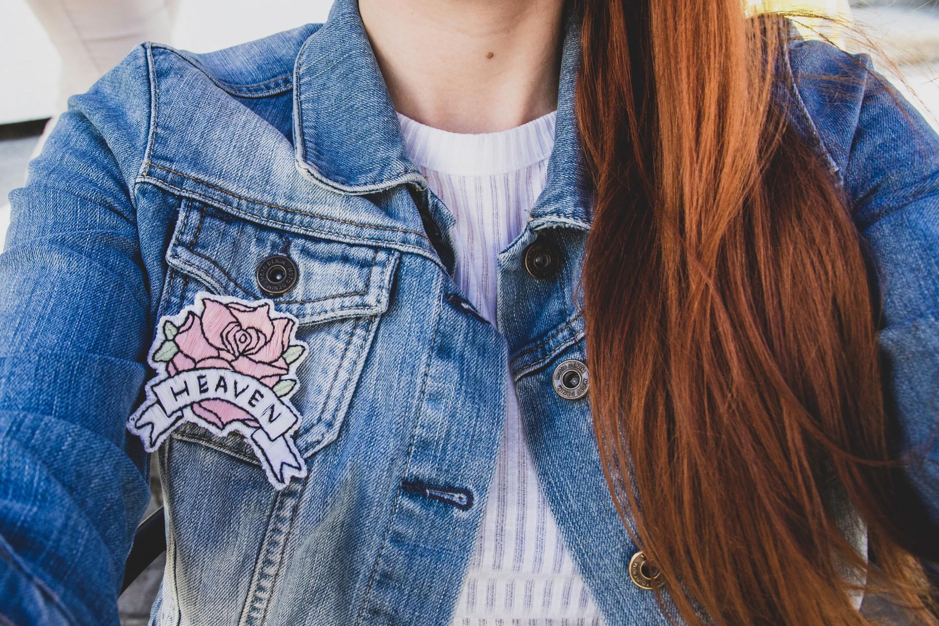 A woman is wearing a denim jacket with a patch on it.