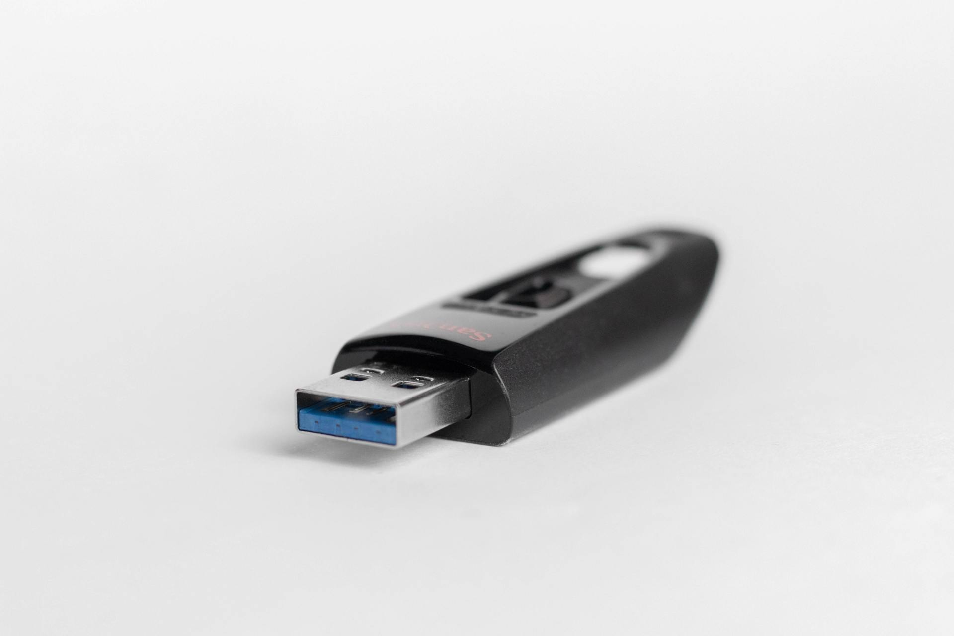 Black USB flash drive with blue port, angled on a white surface.