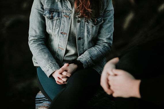 A woman in a denim jacket is sitting on a couch talking to a man.