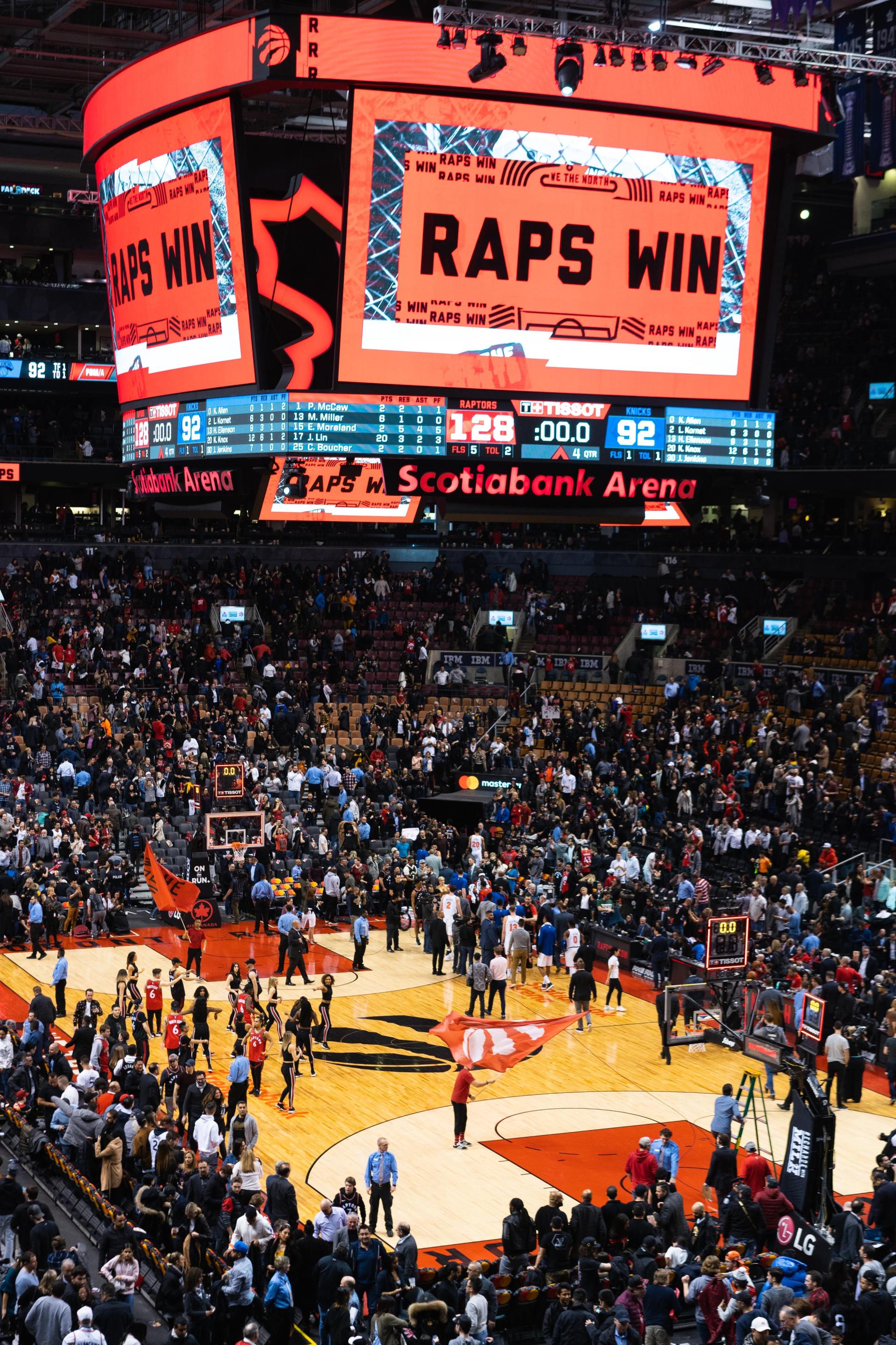 A crowd of people are watching a basketball game with a large screen that says raps win