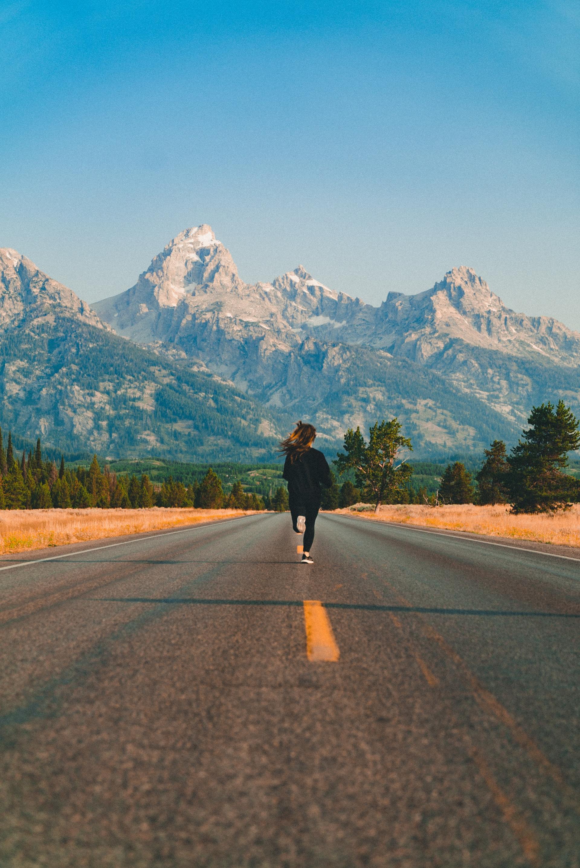 A person is walking down a road with mountains in the background.