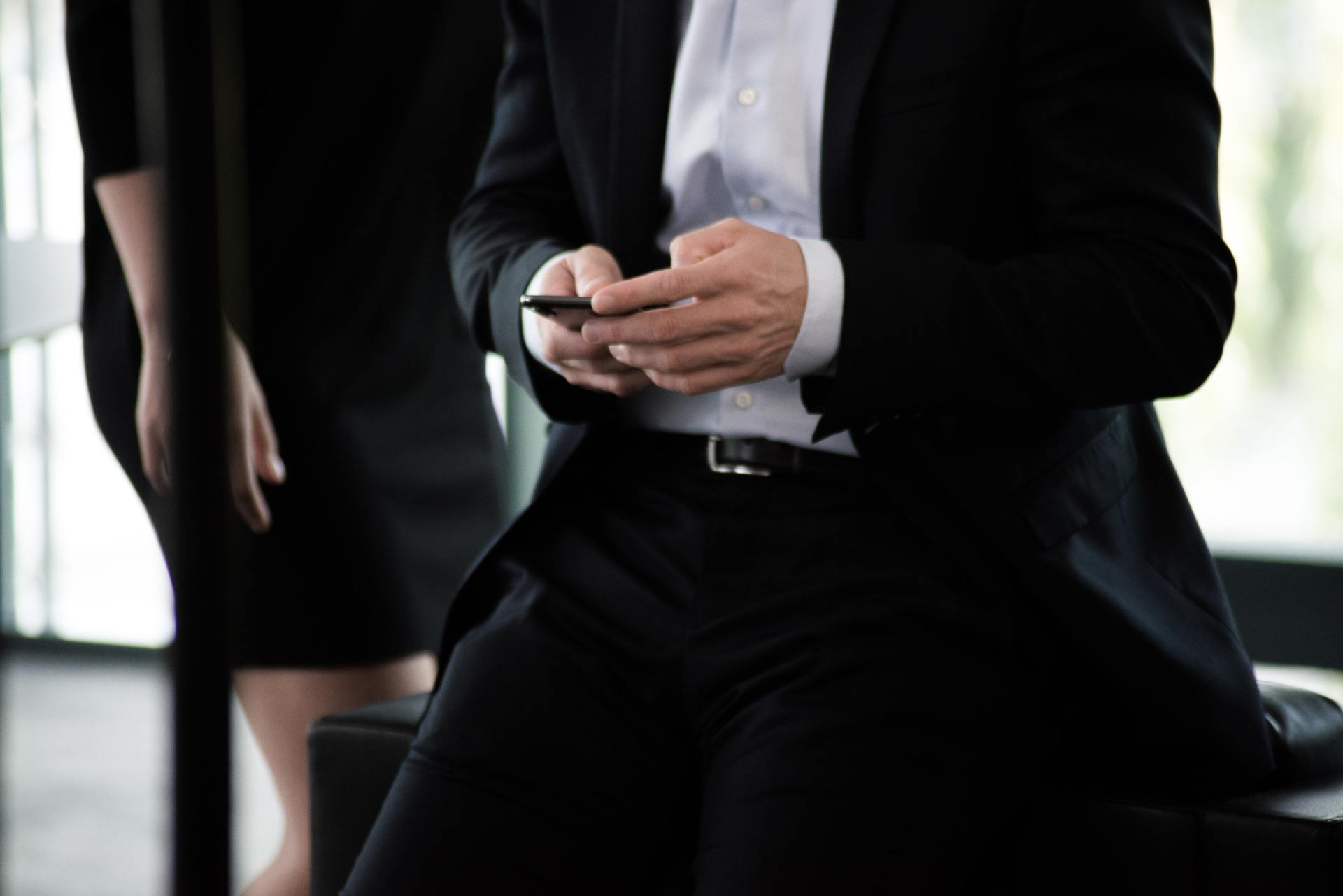 Person in a suit leaning on a desk and using their mobile phone