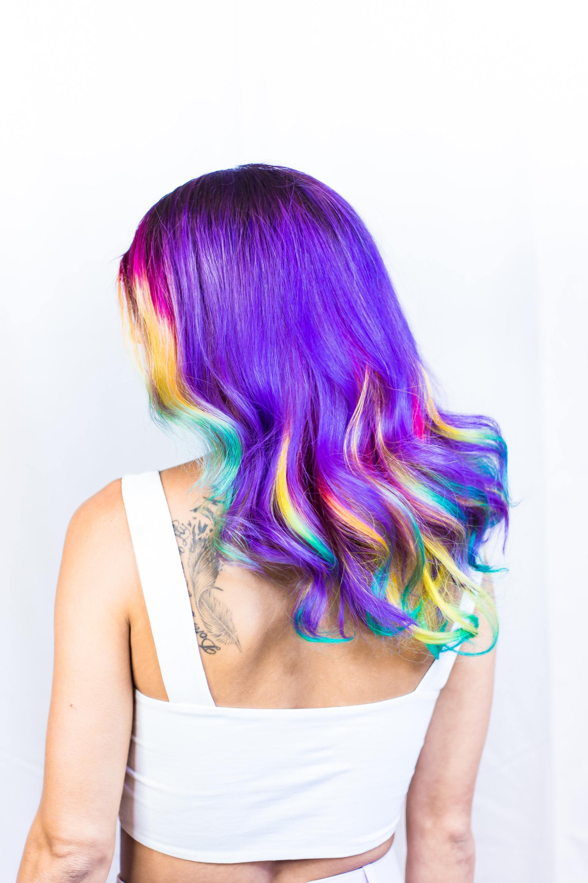 A woman with purple and rainbow hair is wearing a white tank top