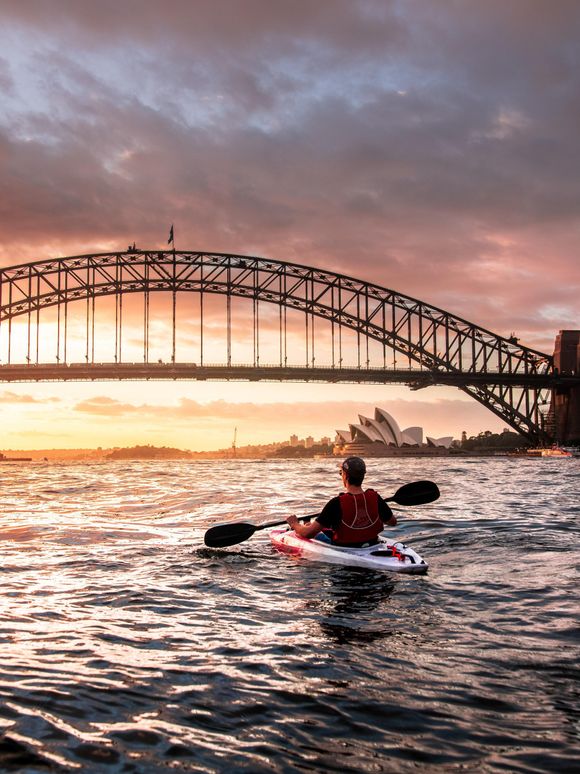 A person in a kayak looking at the Sydney Harbour bridge