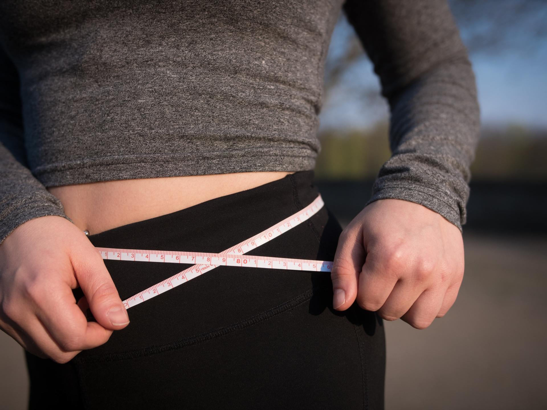 limited view of woman measuring her waist line with tape measure
