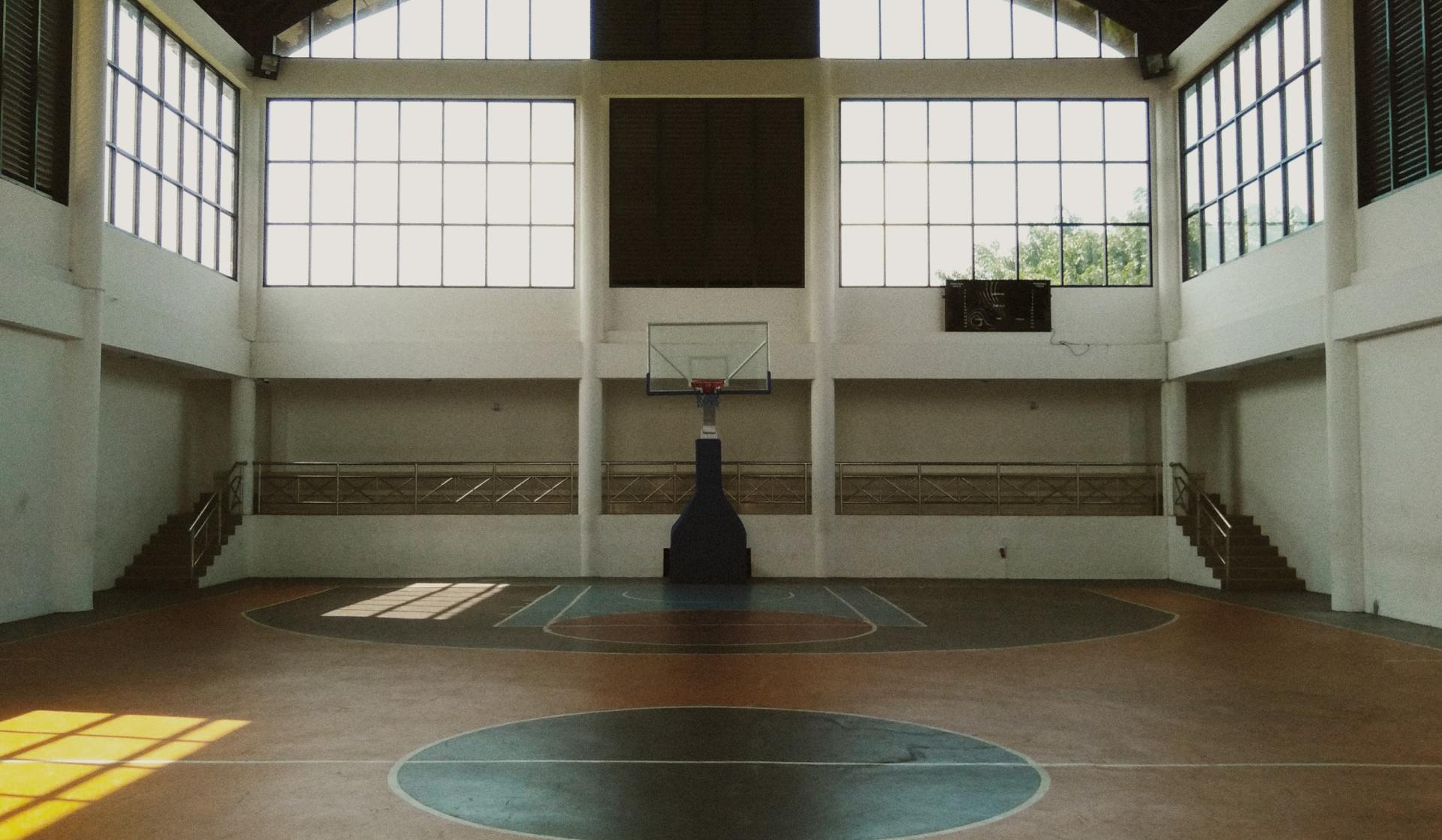 An empty basketball court with a basketball hoop and a large window.