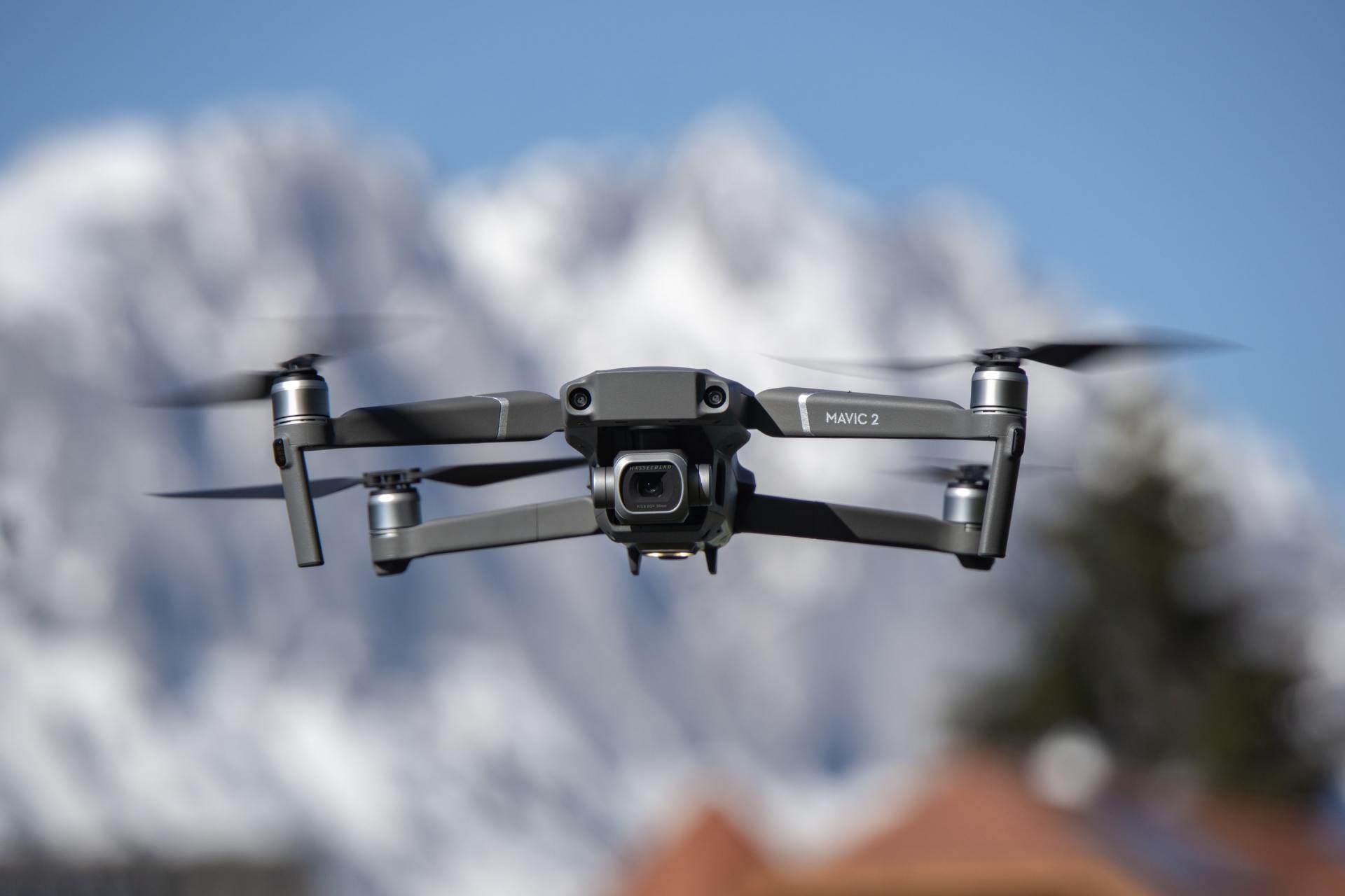 A drone is flying in the sky with mountains in the background.