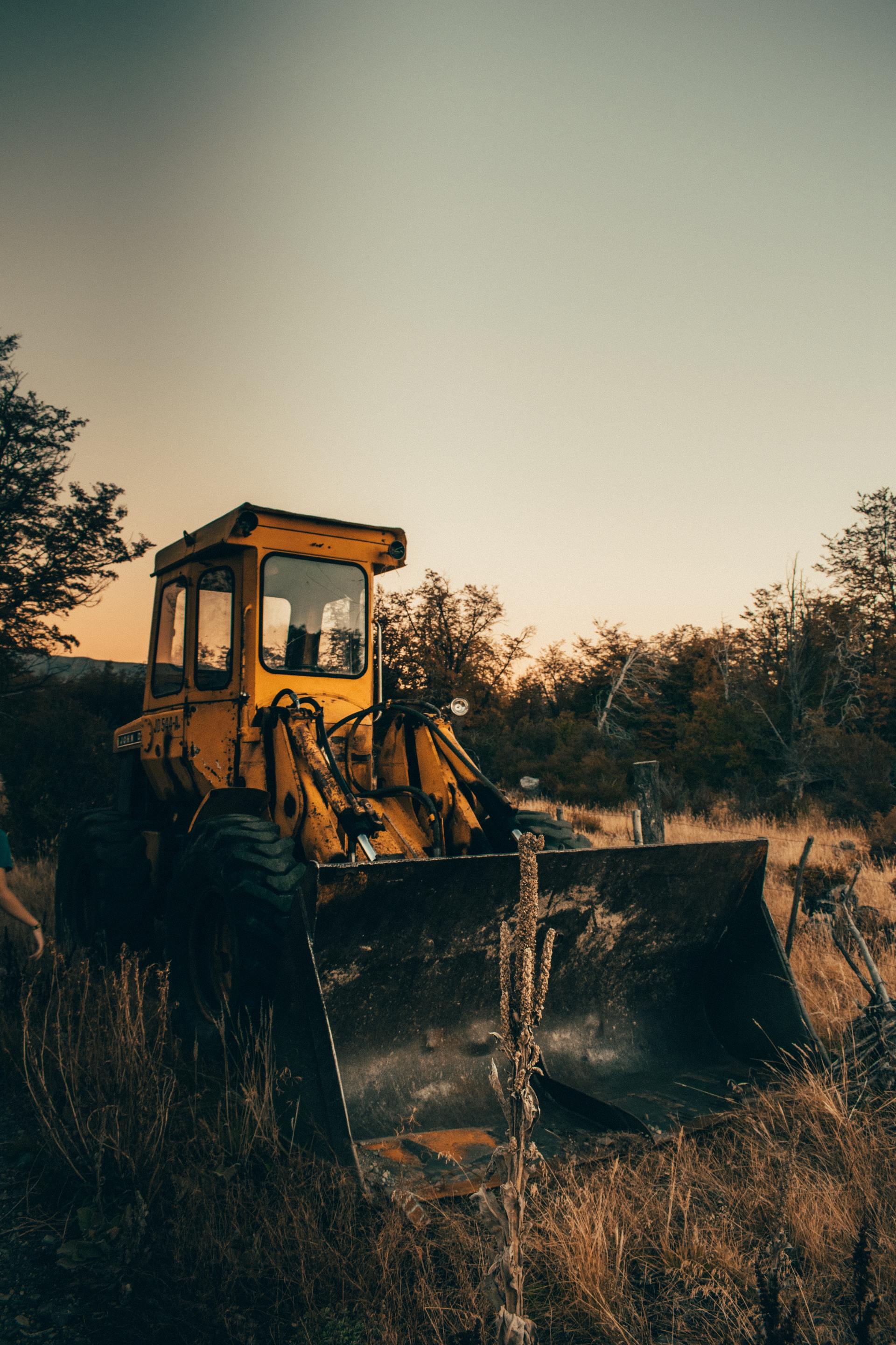 A yellow bulldozer is parked in a field with trees in the background.