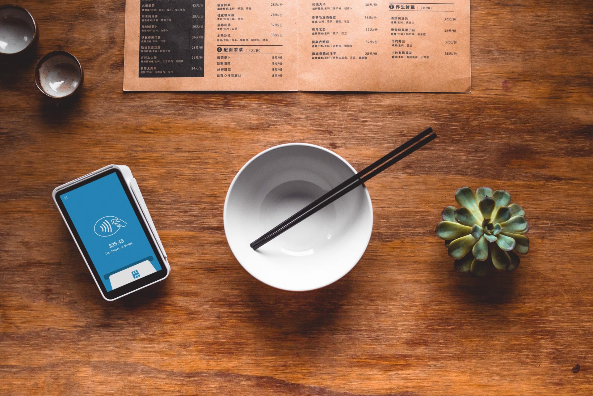 A bowl with chopsticks and a cell phone on a wooden table.
