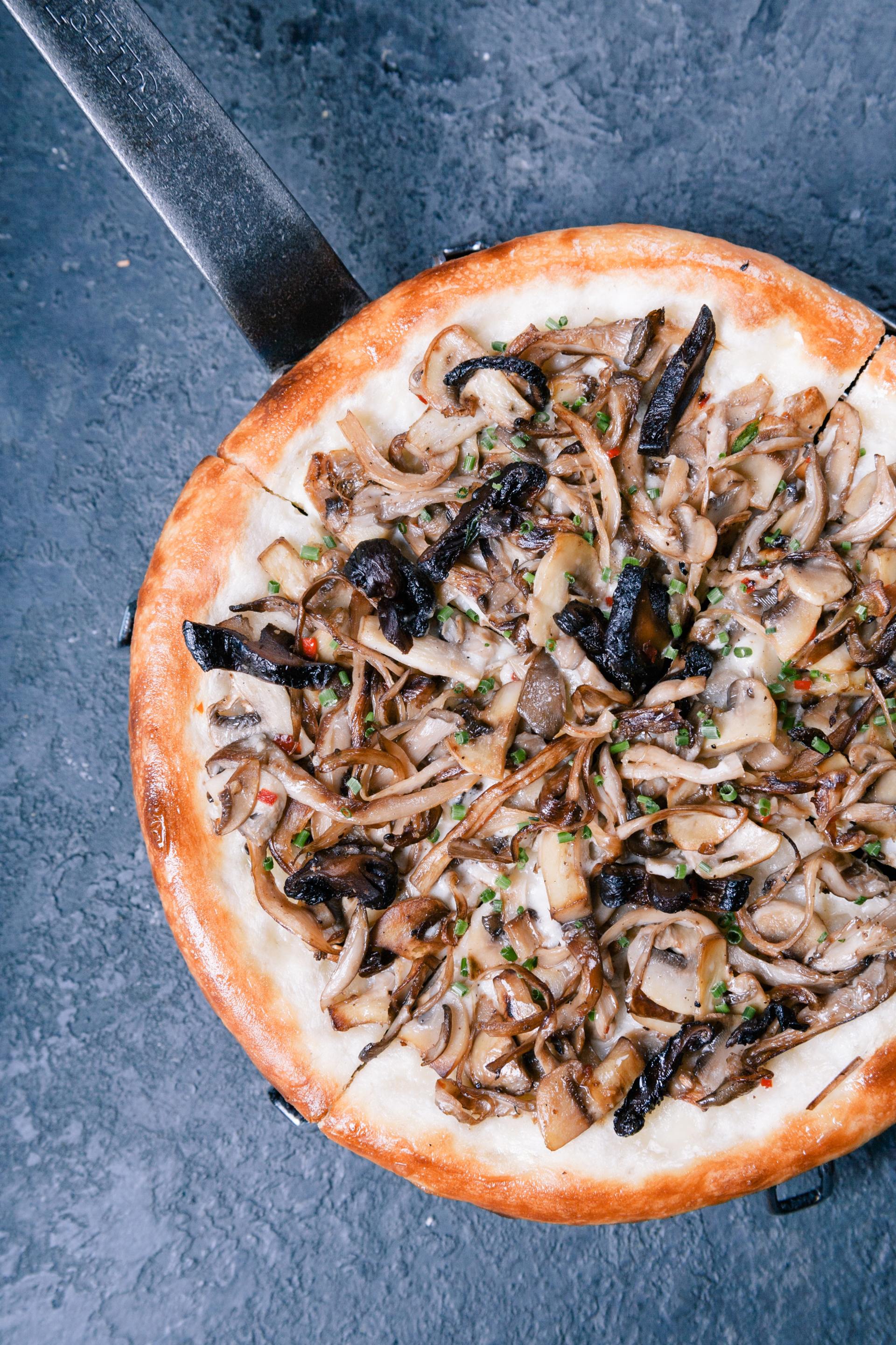 a pizza with mushrooms and onions on a table with a spatula .