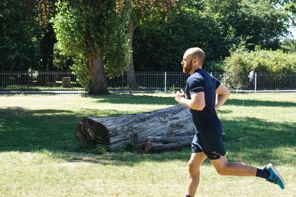 A man is running in a park next to a log.