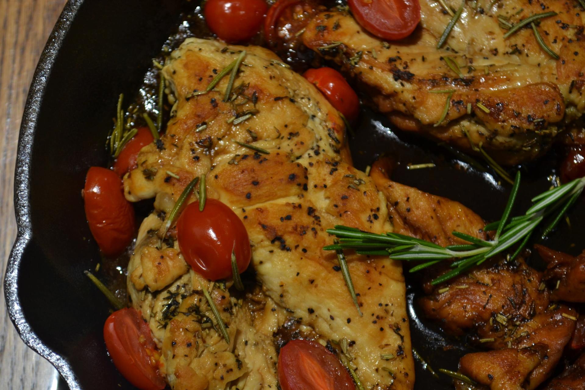 A skillet filled with chicken and tomatoes on a wooden table.