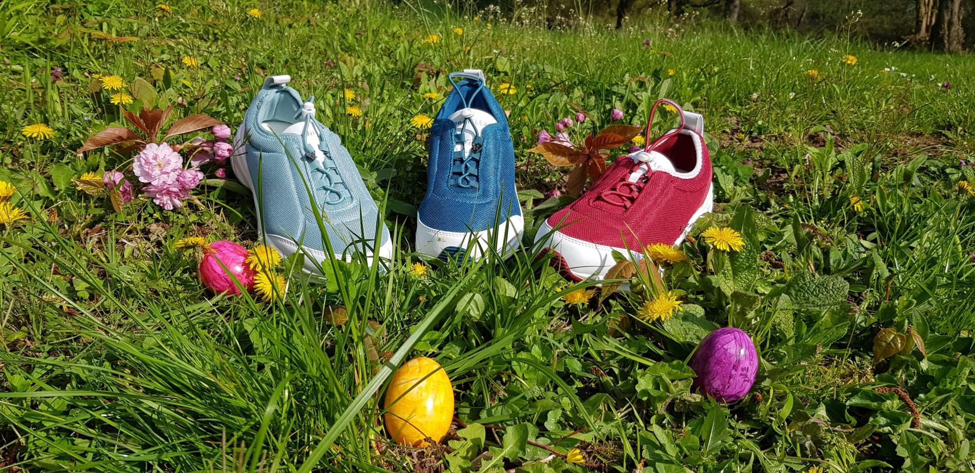 Drei bunte Turnschuhe halten Ostereier auf einer Wiese mit Löwenzahn.
