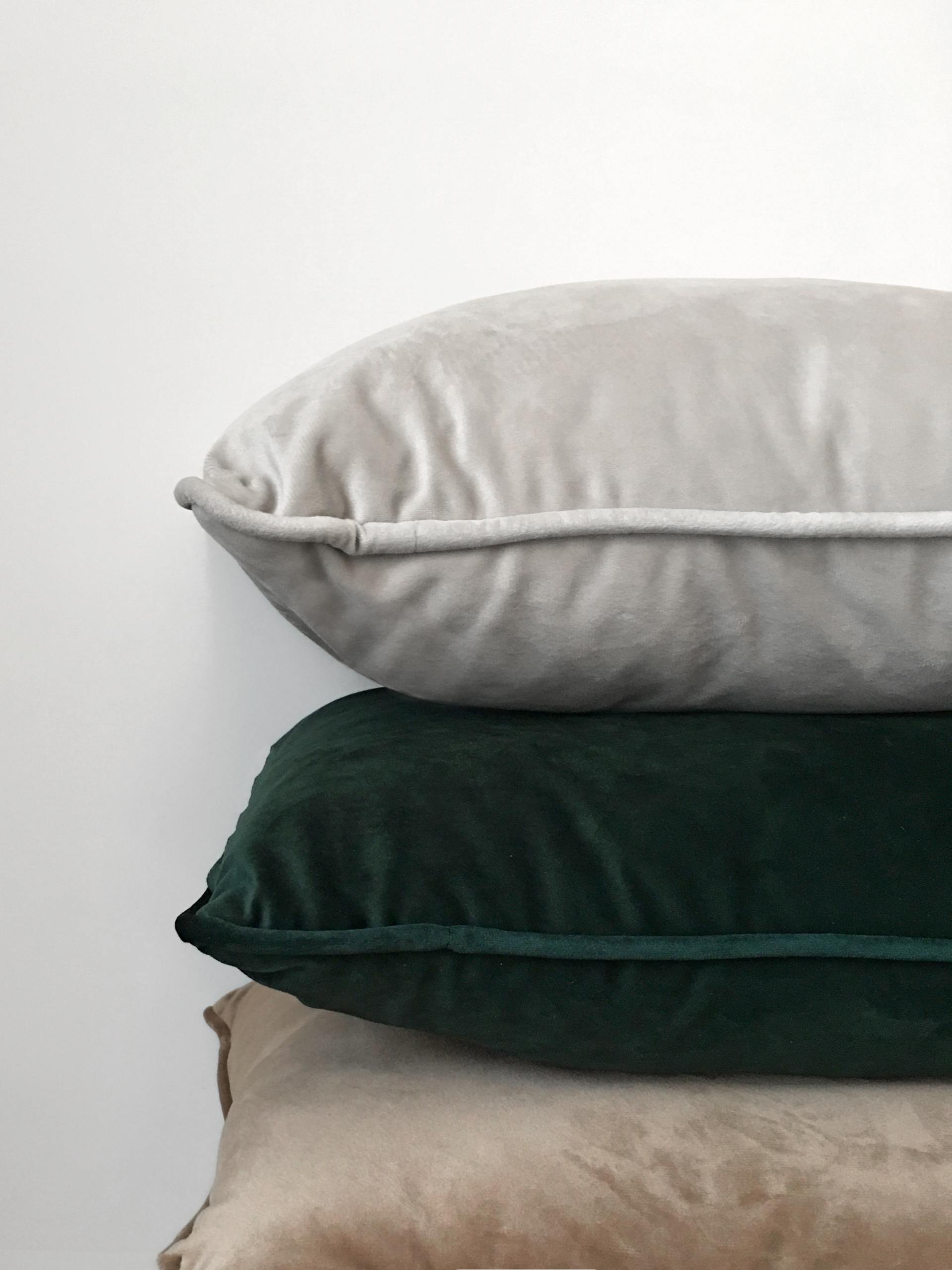 Three velvet pillows stacked, in gray, green, and beige, against a white background.