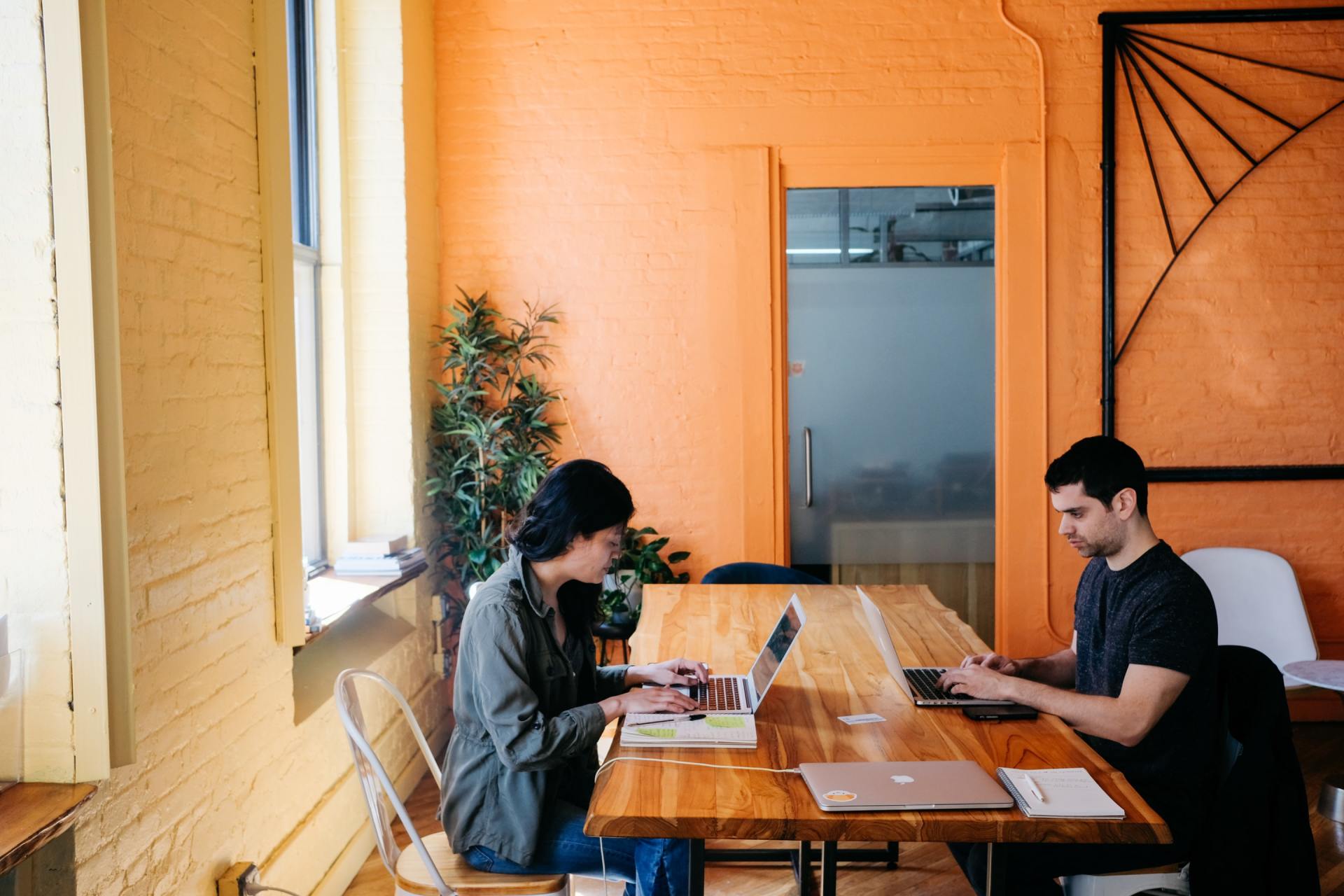 A man and a woman are sitting at a table with laptops.