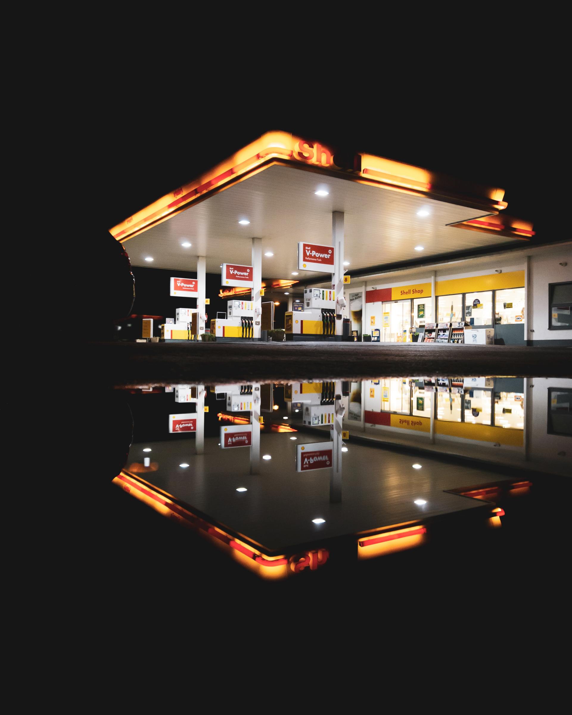 A gas station is reflected in a puddle of water at night