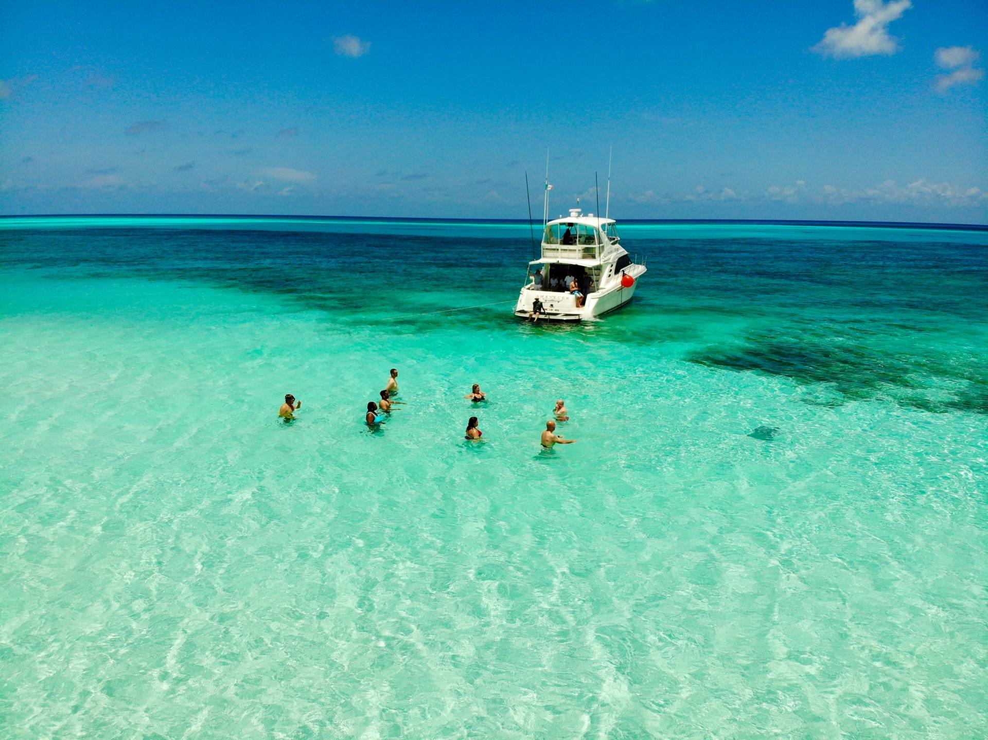 People swimming in clear turquoise water near a boat on a sunny day.