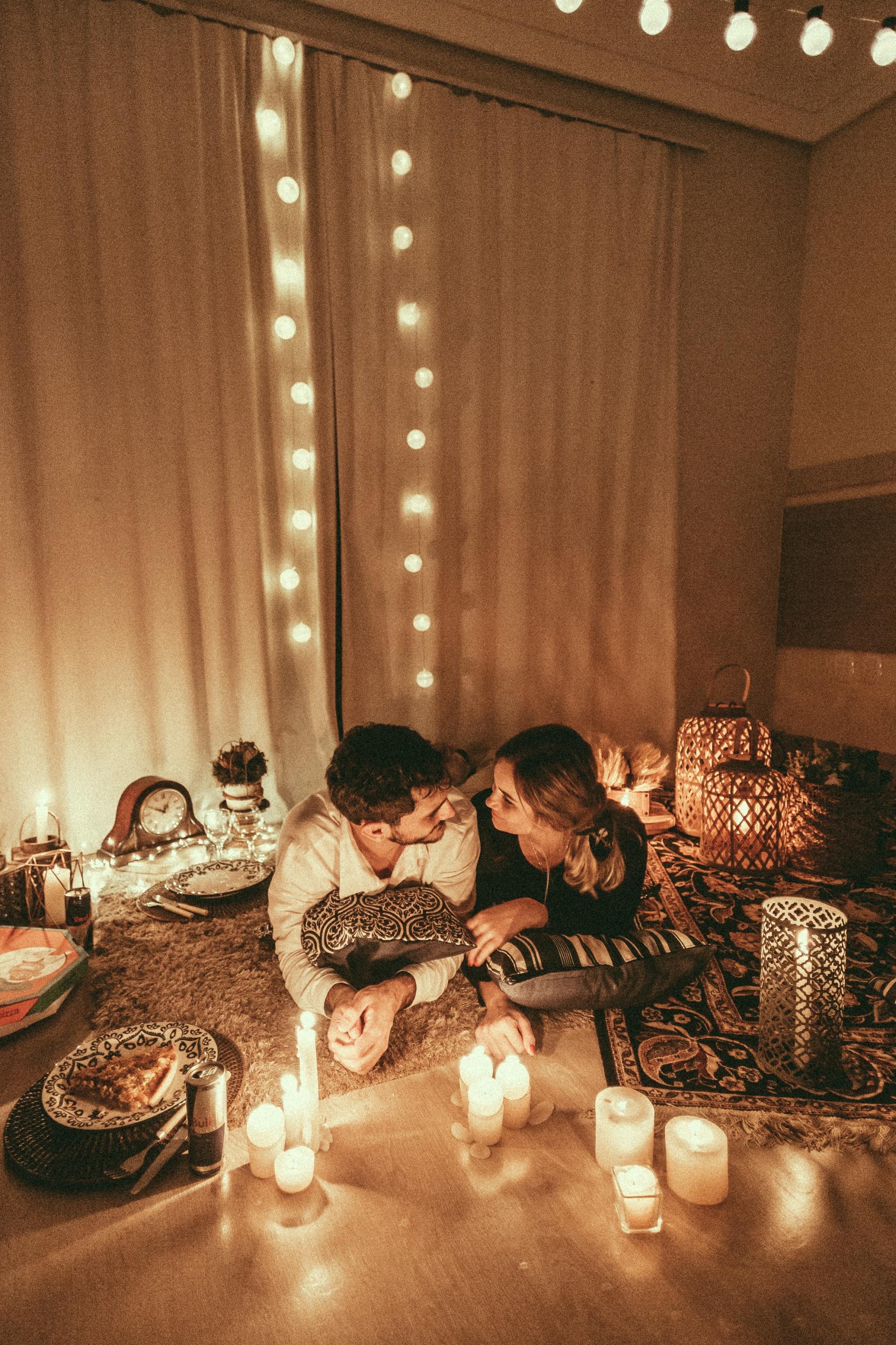 A man and a woman are sitting on the floor in a living room surrounded by candles.