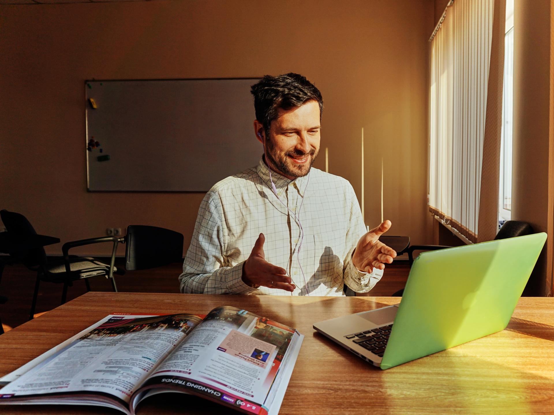 A man is sitting at a table with a laptop and a magazine.