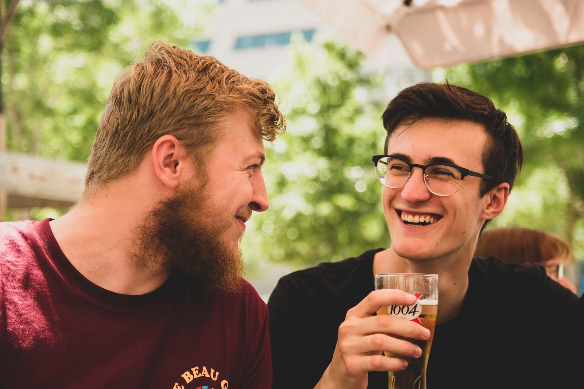 Two men sitting next to each other drinking beer and laughing.