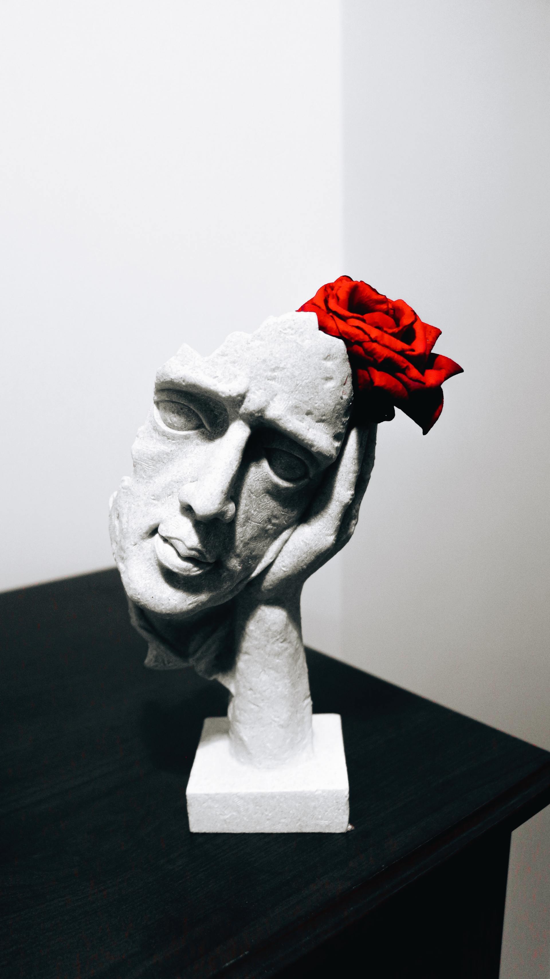 A statue of a man with a red rose on his head.