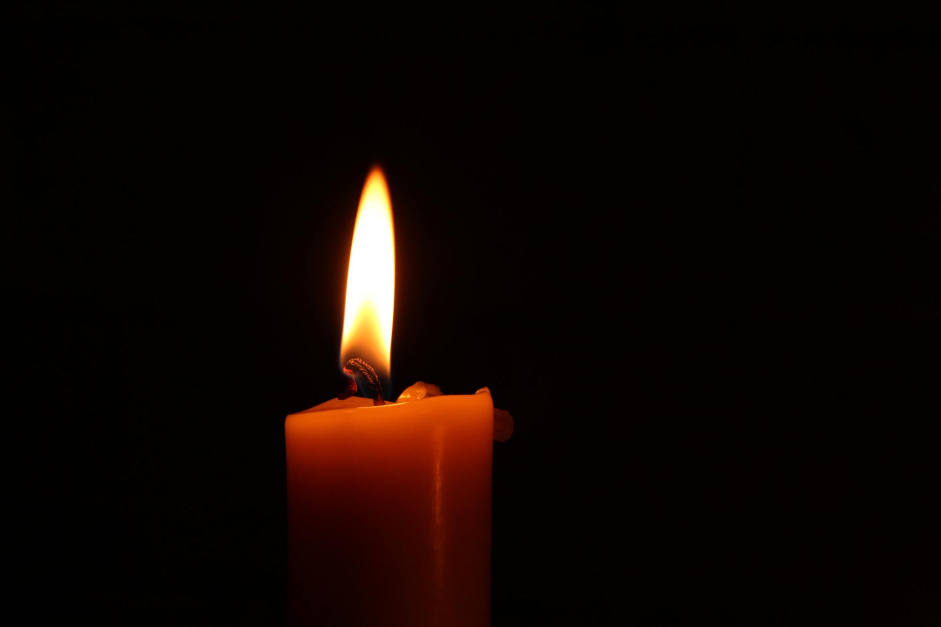 A close up of a lit candle in the dark.