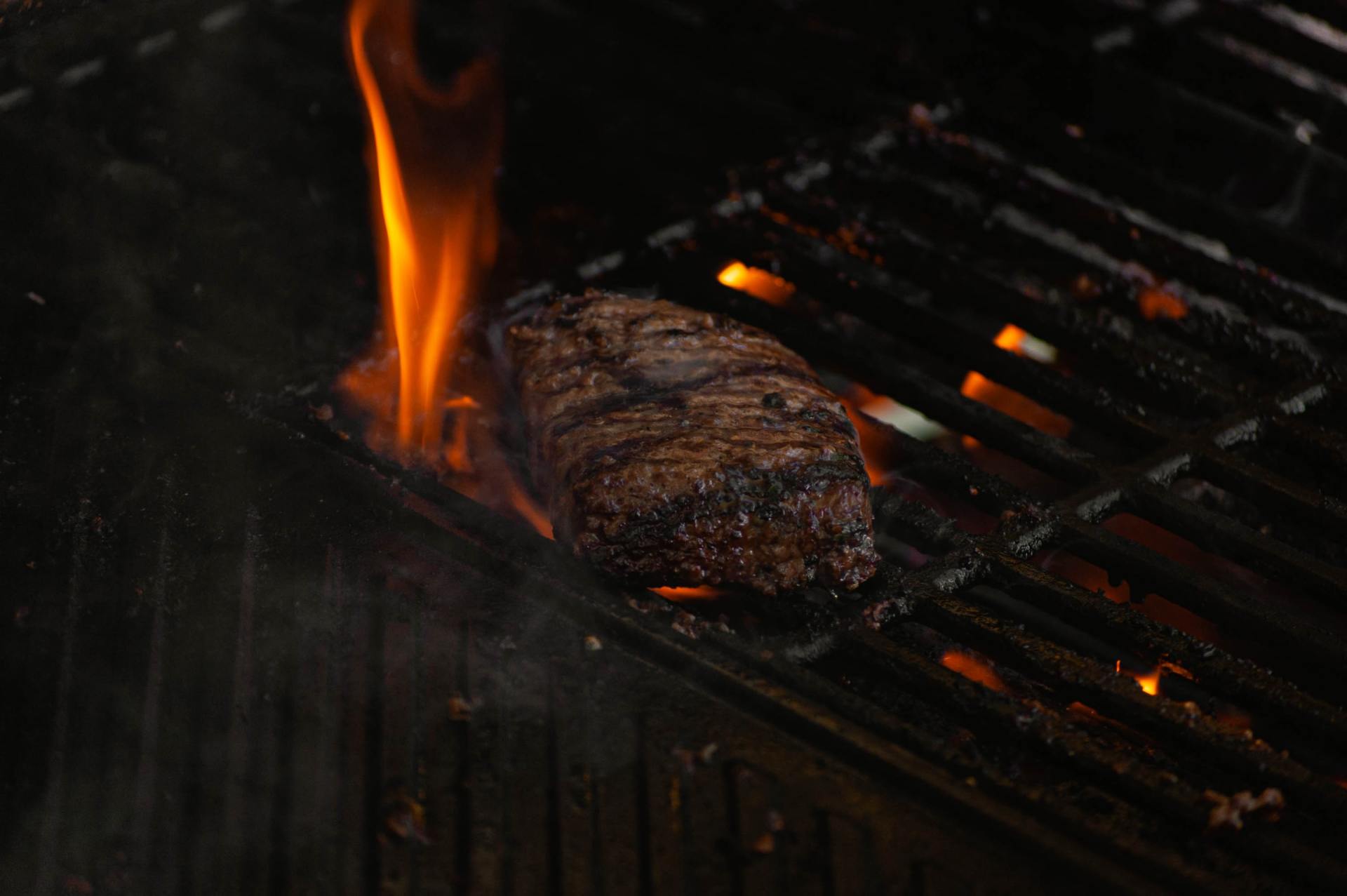 A steak is cooking on a grill with flames coming out of it.