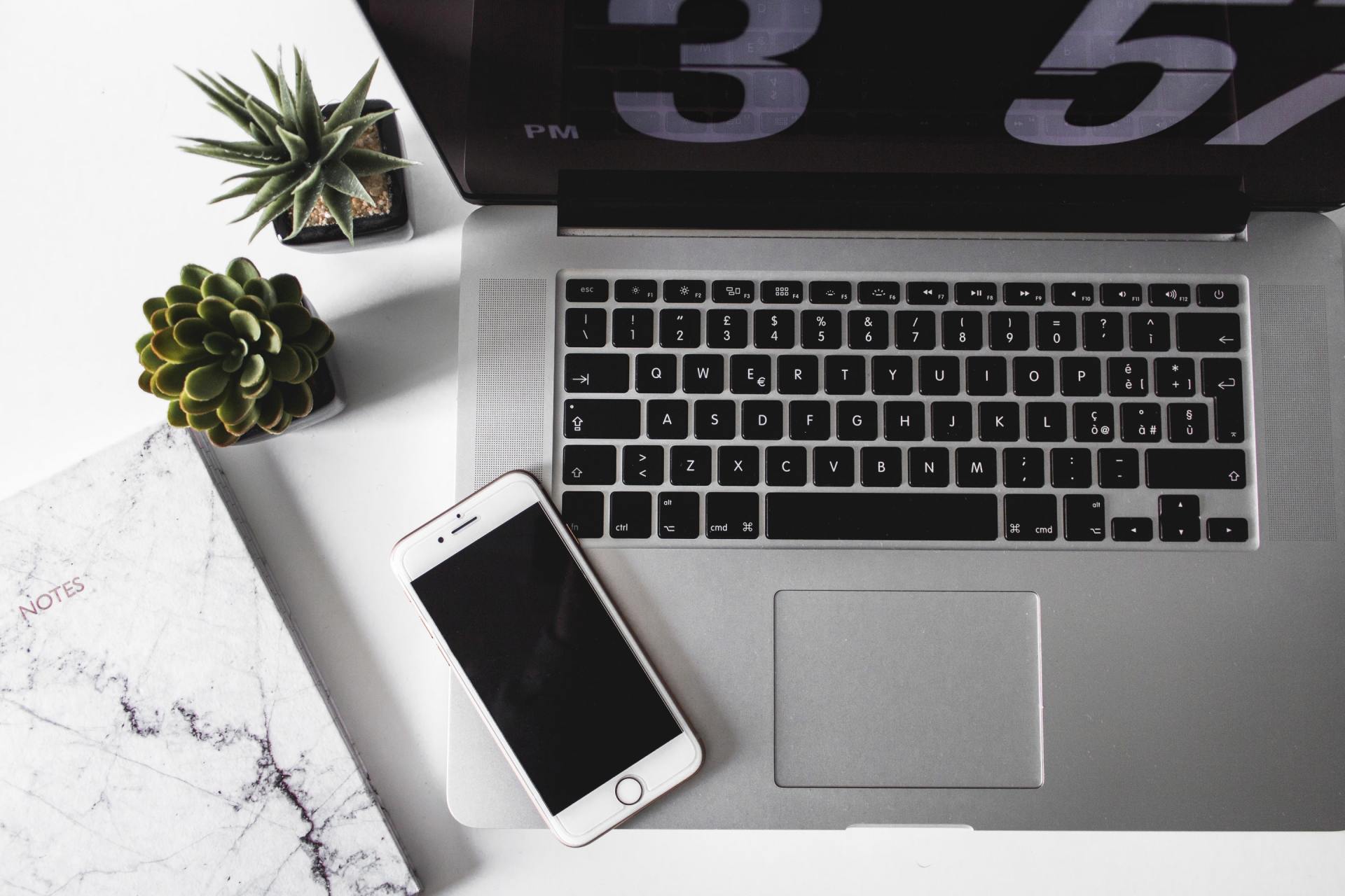 A laptop and a cell phone on a desk with a clock that says 3:55