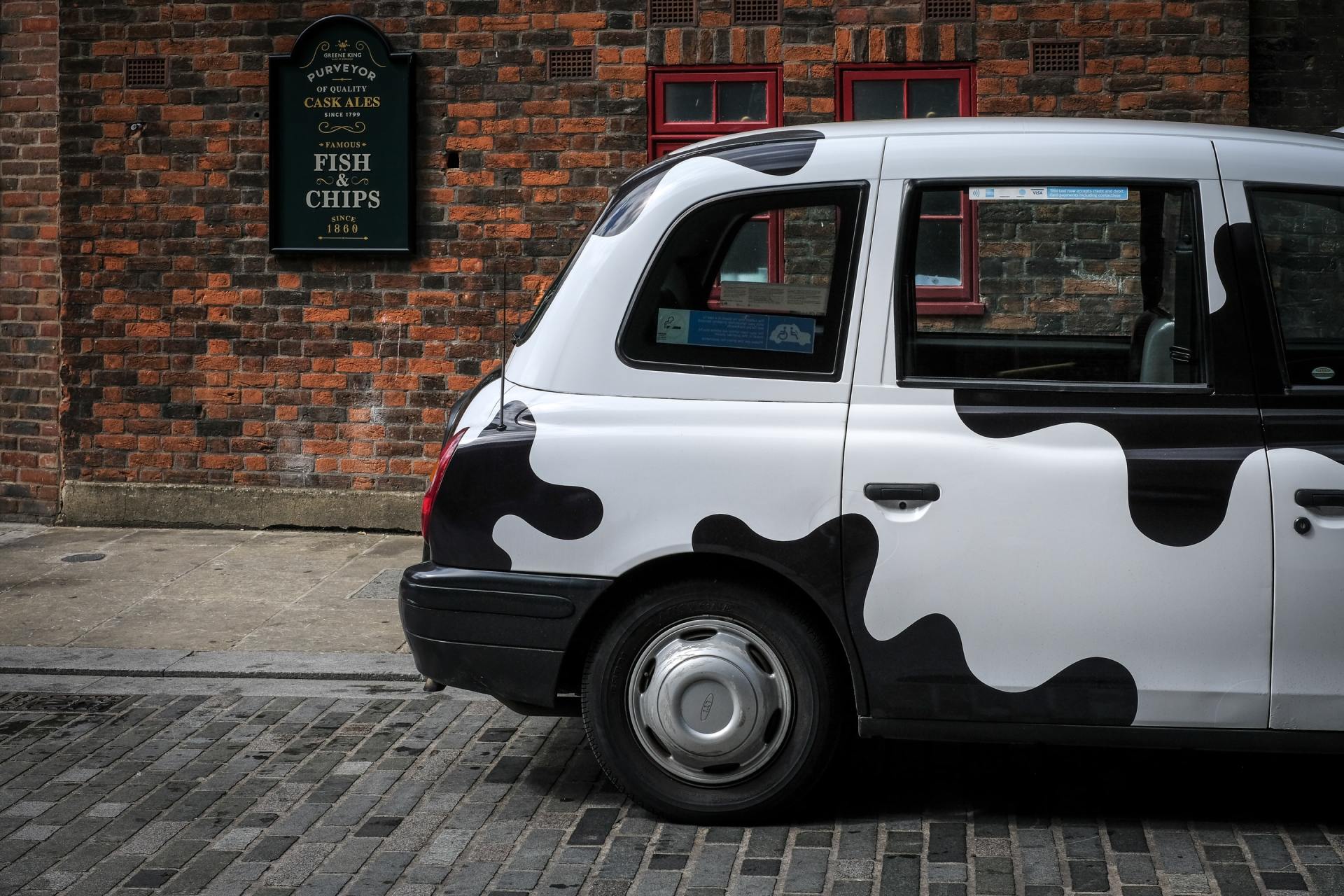 a black and white cow print taxi cab is parked in front of a brick building .